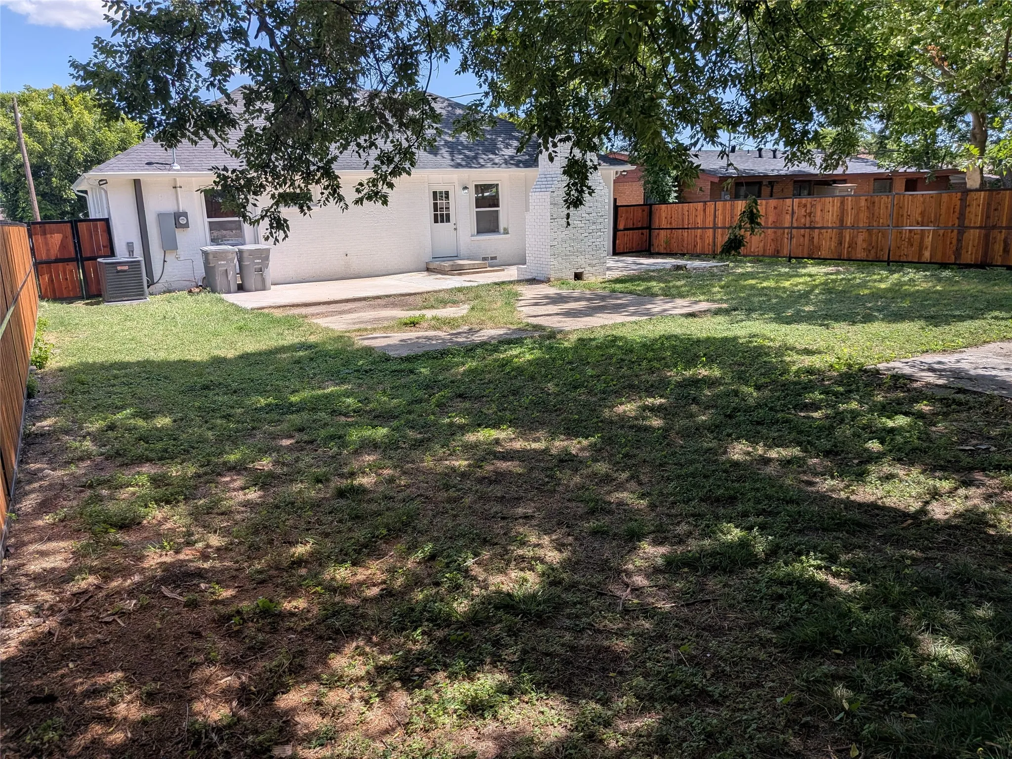 Expansive backyard featuring a partial privacy fence with wood-panel and metal sections, a concrete patio area, and a white exterior wall