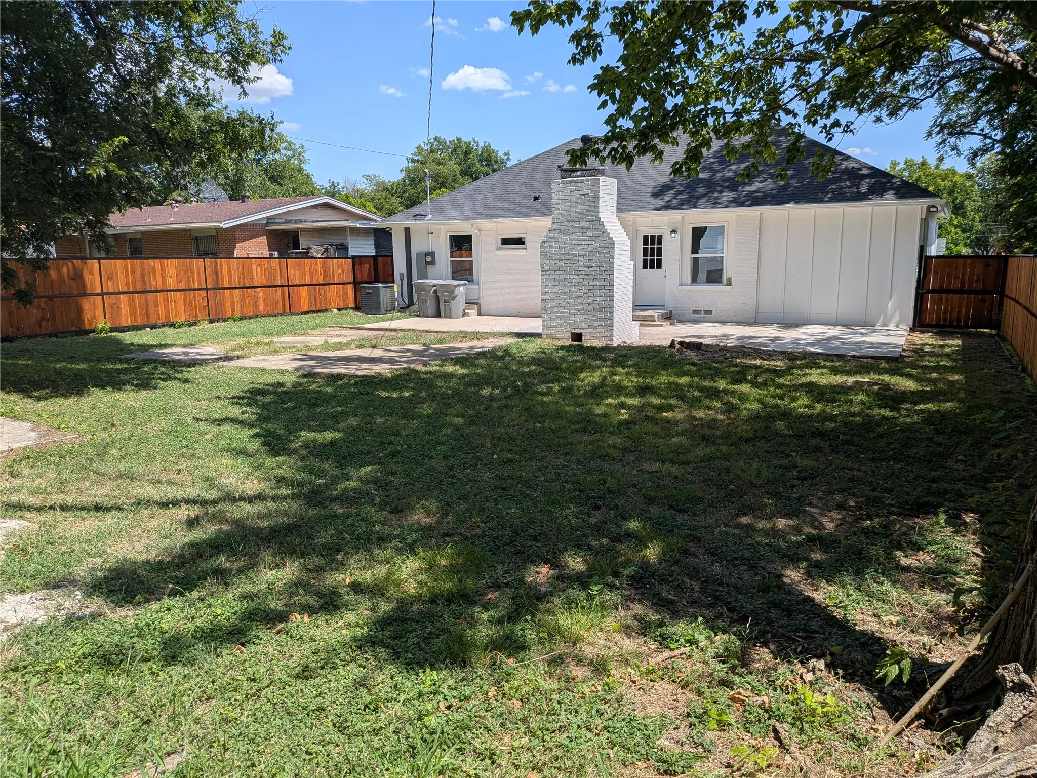 Expansive backyard featuring a new wood privacy fence, concrete patio, and a white brick exterior