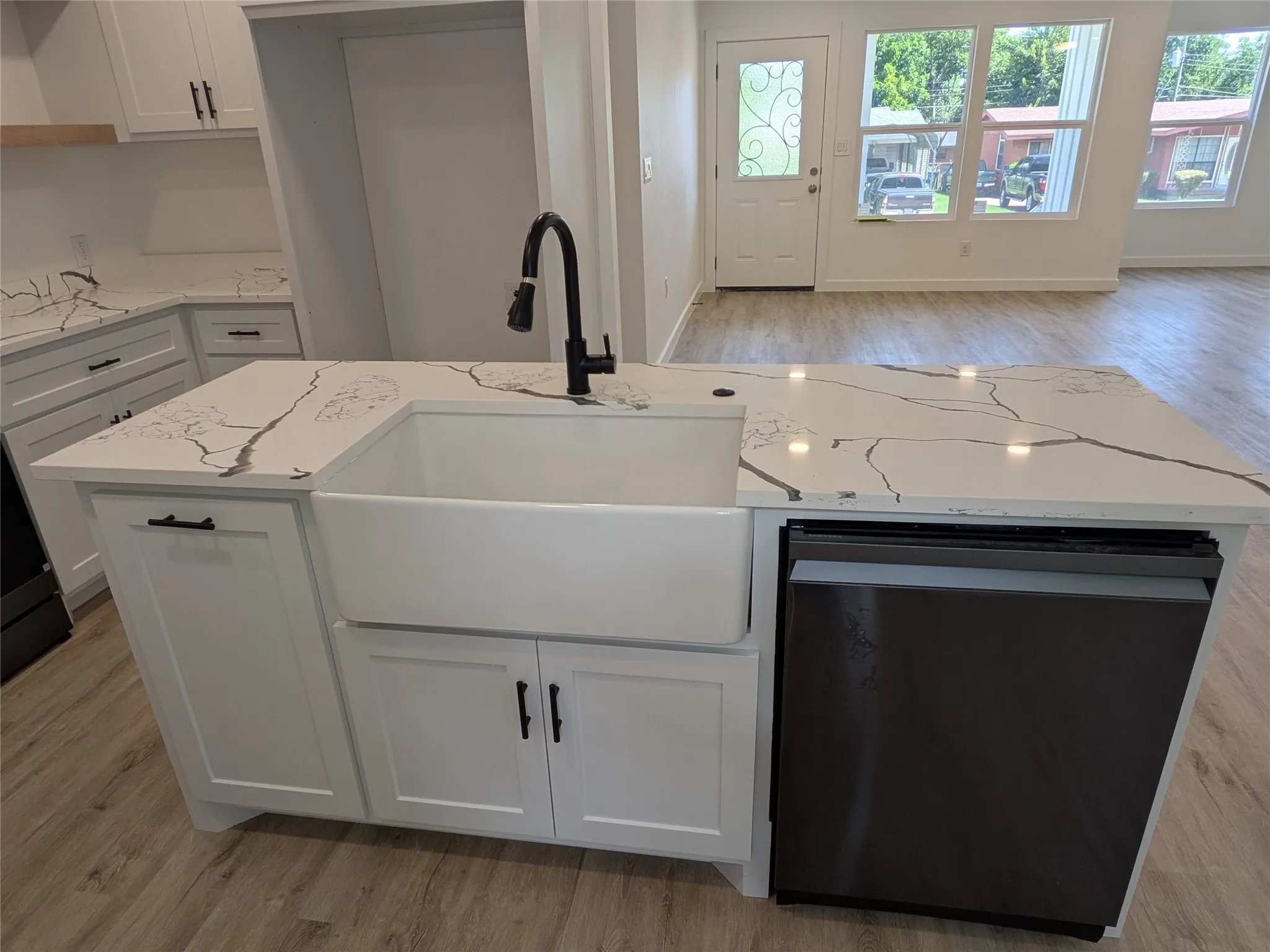 Kitchen island with a farmhouse sink and matte black faucet, featuring white cabinetry, a dishwasher with a dark panel, and white countertops with dark veining
