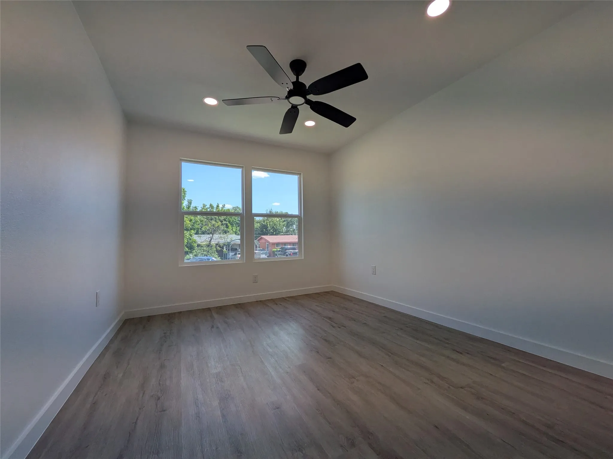 Spacious interior room featuring wood-finish flooring, recessed lighting, and a modern ceiling fan