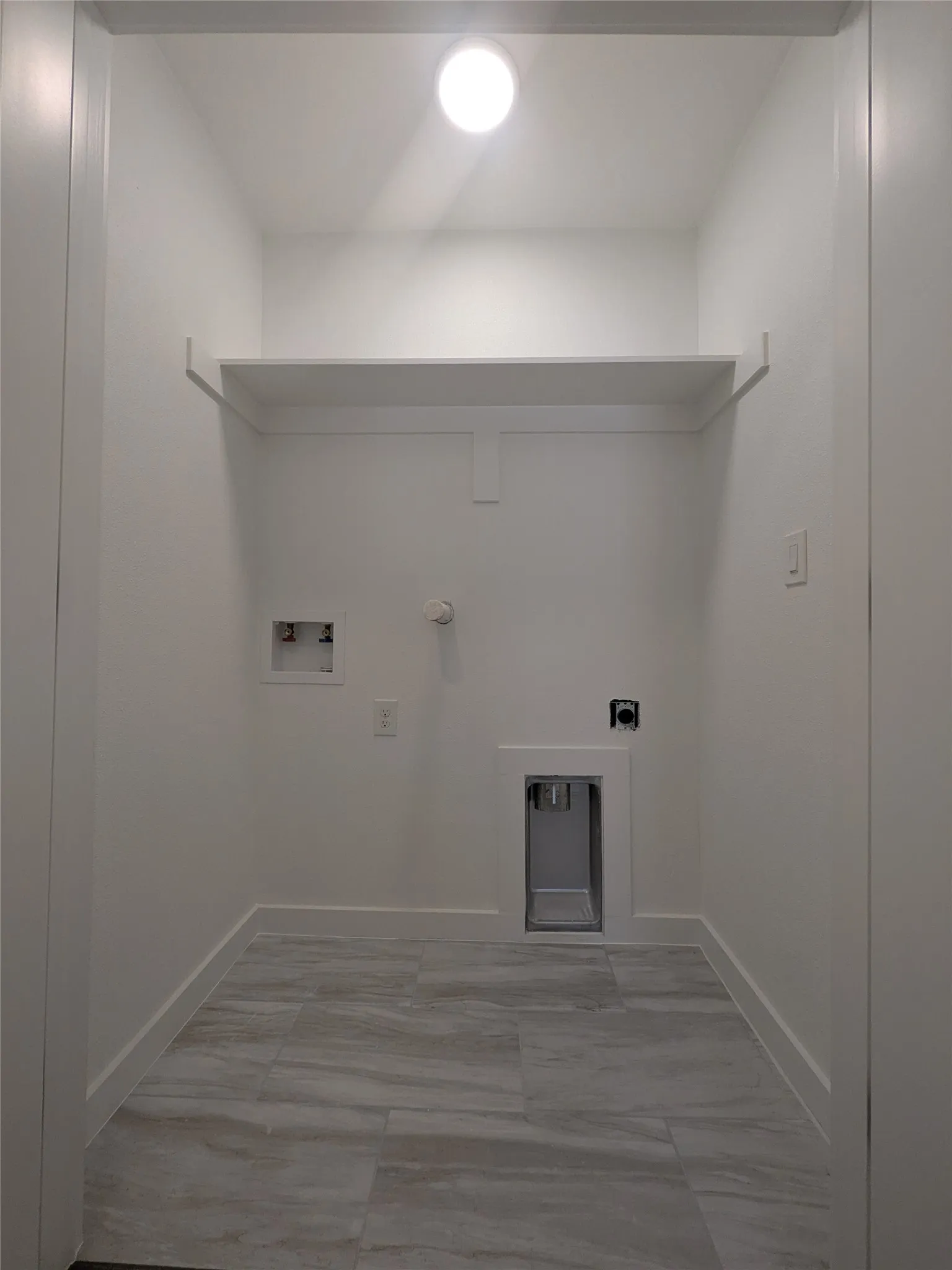 Dedicated laundry area featuring marble-finish tile flooring, a recessed dryer vent, and a built-in storage shelf