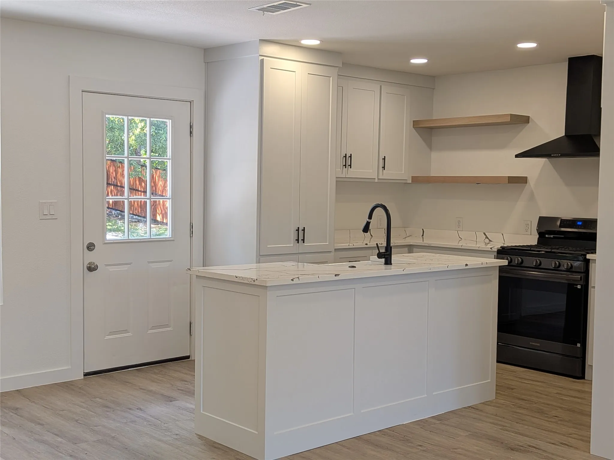 Modern kitchen featuring white shaker cabinetry, an island with integrated sink and matte black faucet, and stone-finish countertops