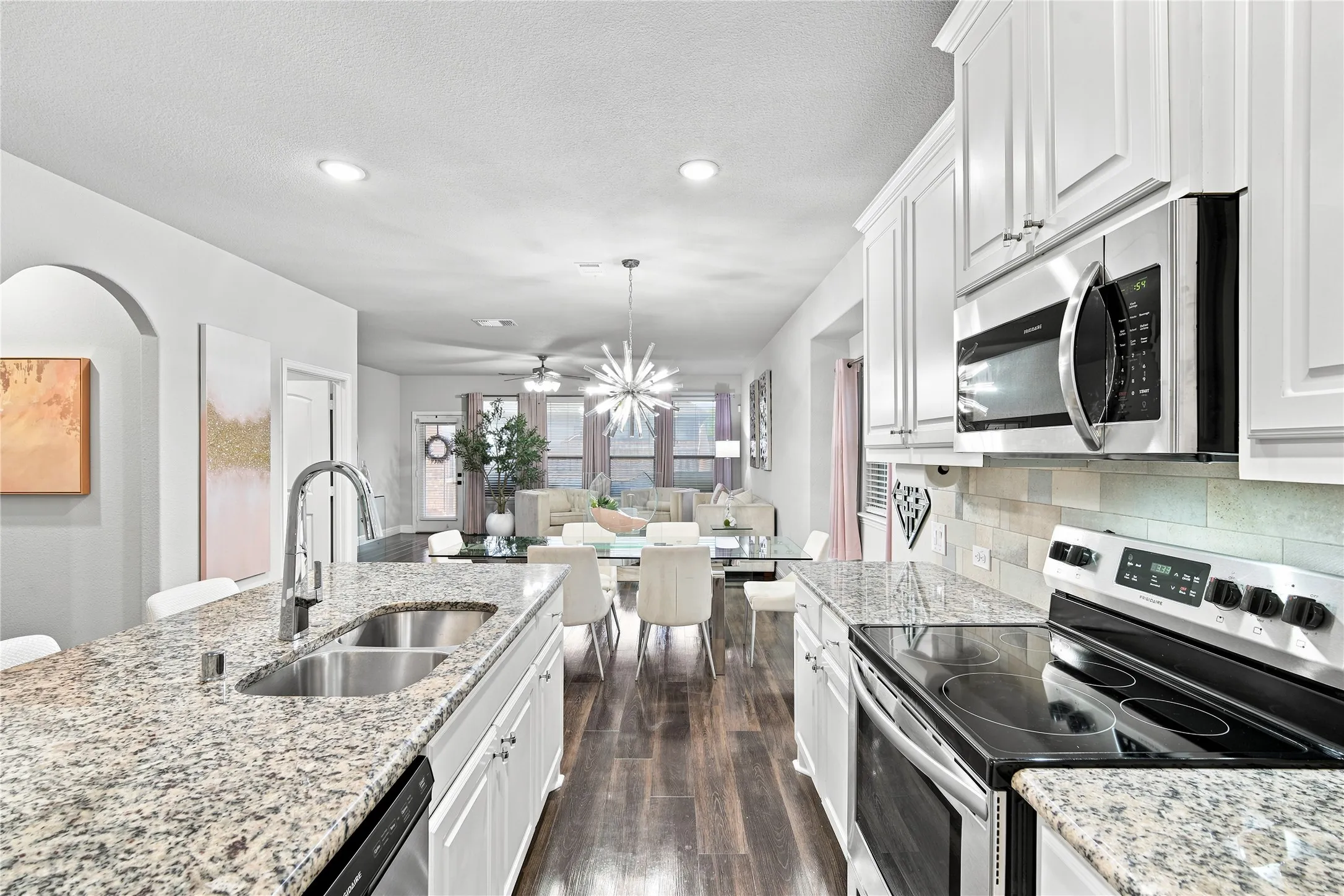 Kitchen featuring granite countertops, stainless steel appliances, white cabinetry, a double basin sink, and wood-finish flooring