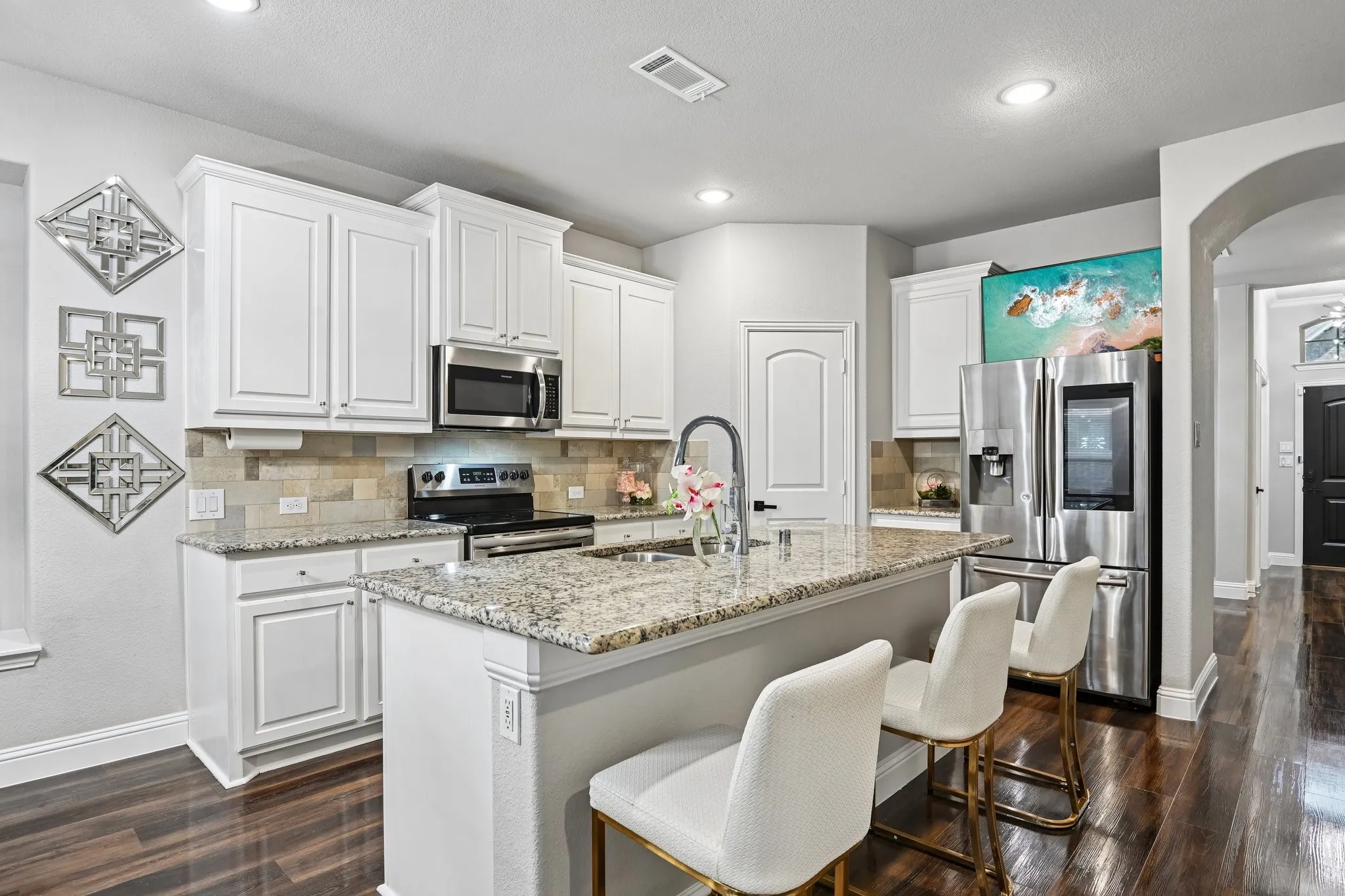 Open-concept kitchen featuring white cabinetry, granite countertops, stainless steel appliances, a tile backsplash, and a central island with a built-in sink