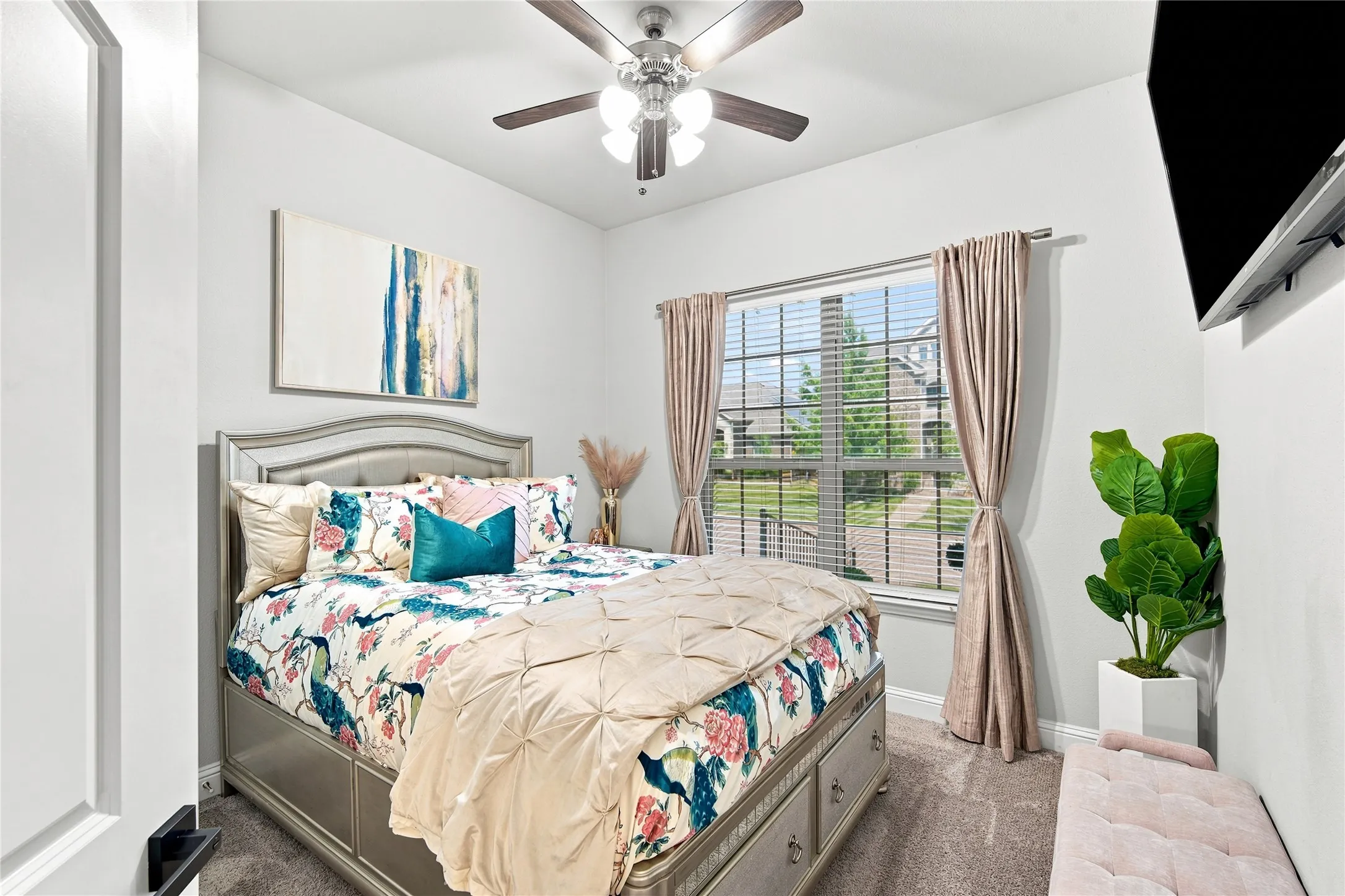 Carpeted room featuring a ceiling fan with light fixture, a window with blinds and drapes, and a wall-mounted flat-screen bracket