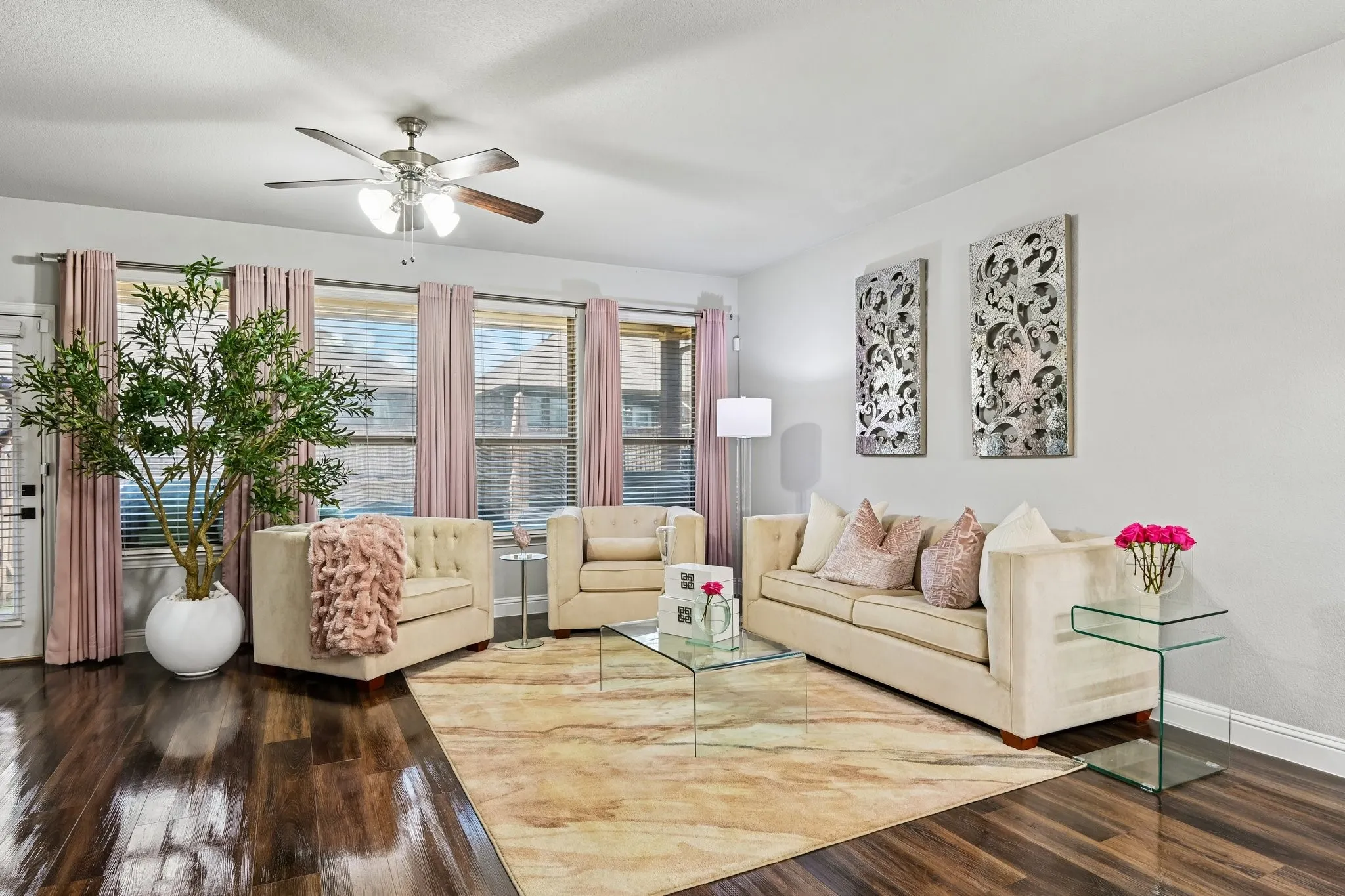 Spacious living area featuring wood-finish flooring, a ceiling fan with integrated lighting, and multiple windows providing ample natural light