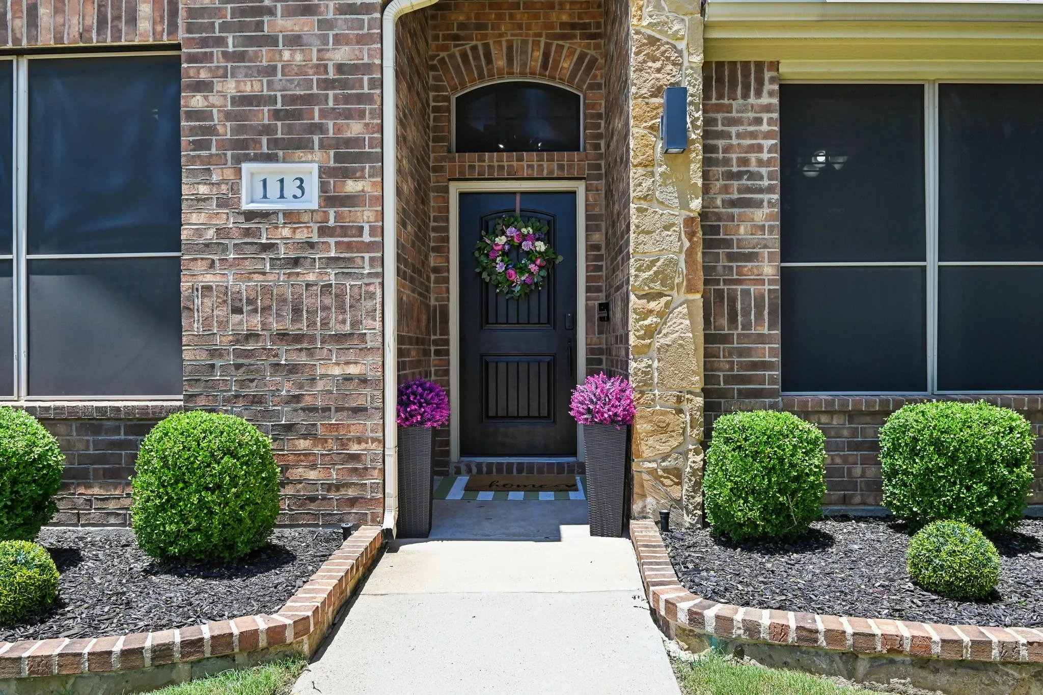 Brick and stone facade featuring a dark wood-finish front door with an arched transom