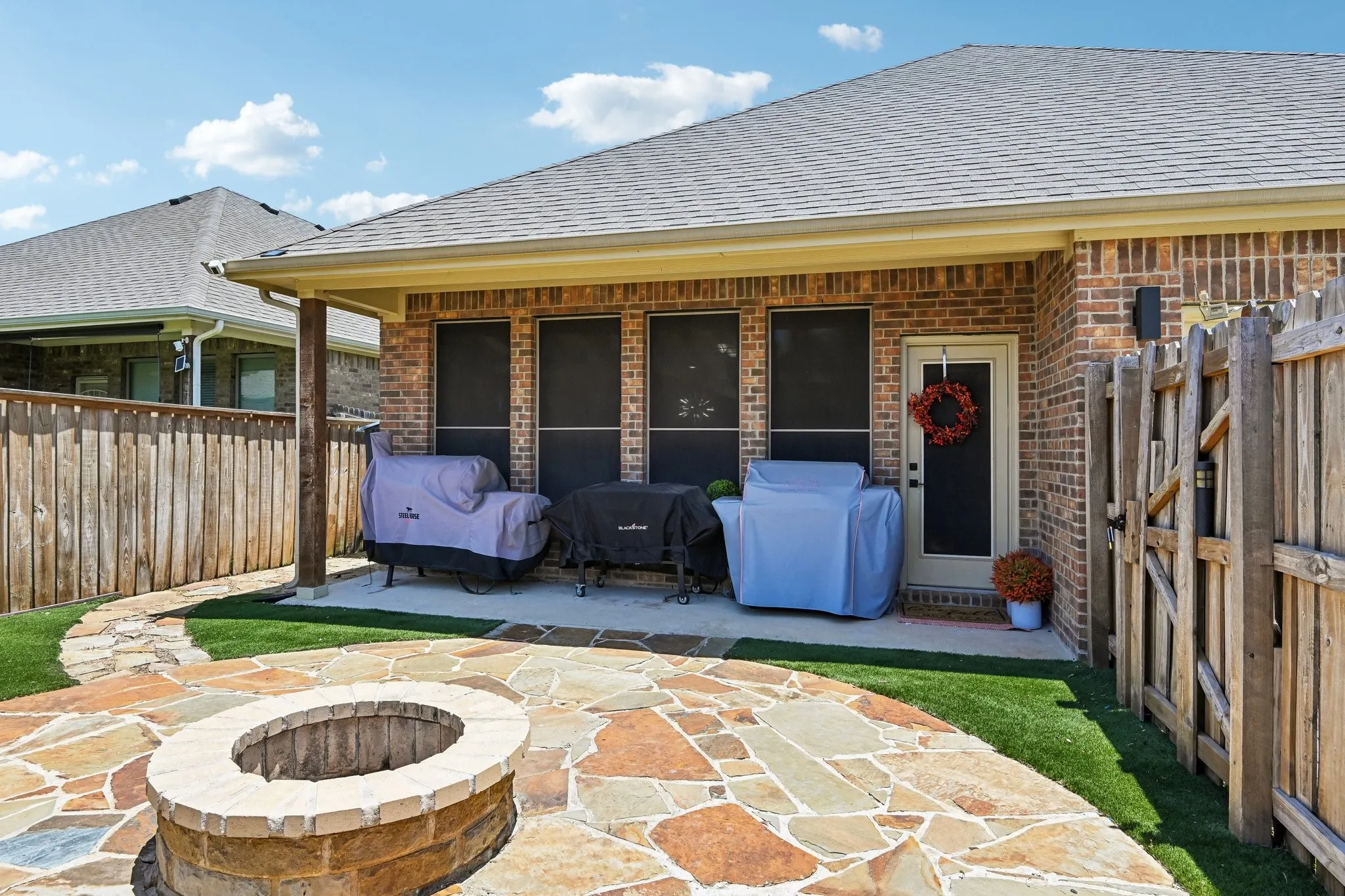 Outdoor living space featuring a flagstone patio, built-in fire pit, covered concrete patio, brick exterior, and a wood privacy fence