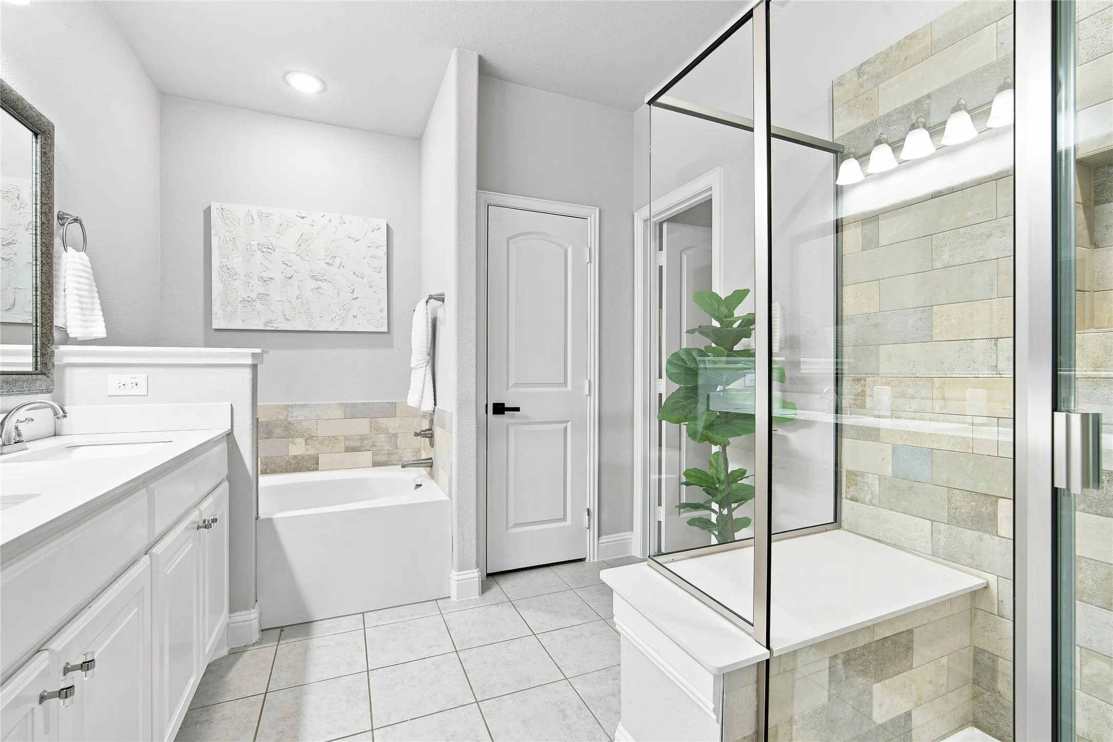 Bathroom featuring a dual vanity, white cabinetry with silver hardware, a built-in tub with tile surround, a walk-in shower with a built-in bench, and a tile floor
