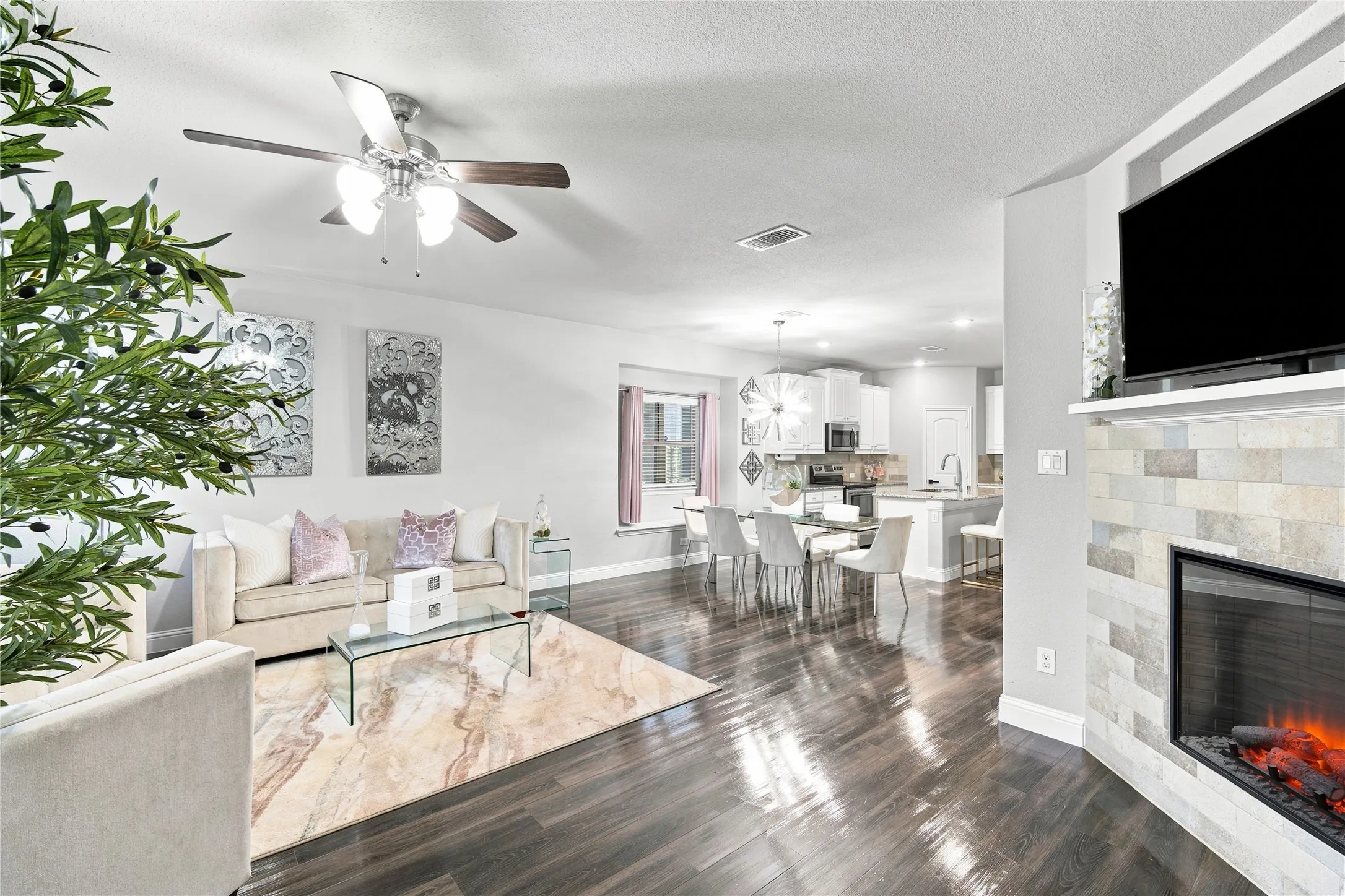 Expansive living area featuring rich wood-finish flooring, a contemporary ceiling fan, and a stone-clad fireplace with a mantel