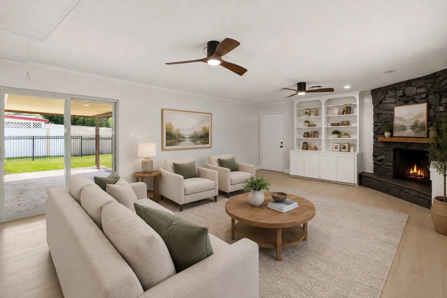 Expansive living room featuring a stone-clad fireplace with a wood mantel, built-in shelving, wood-finish flooring, and sliding glass doors opening to a covered patio
