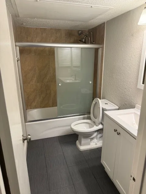 Full bathroom featuring tile flooring, toilet, vanity, and shower / bath combination with glass door