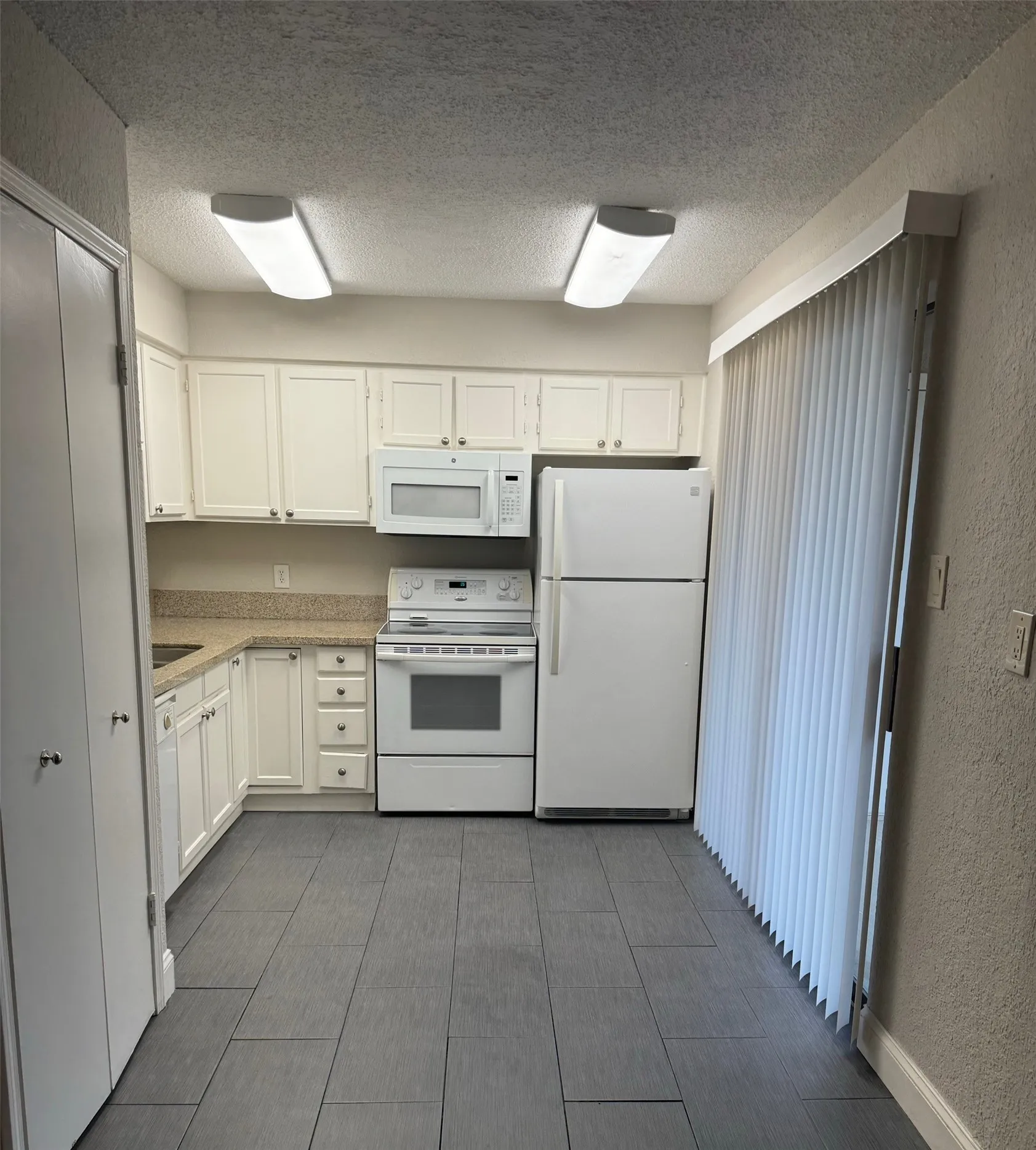 Kitchen with white cabinets, tile floors, white appliances, stackable washer & dryer in utility closet, balcony off kitchen and all open to the spacious Living Room with Fireplace, perfect for entertaining