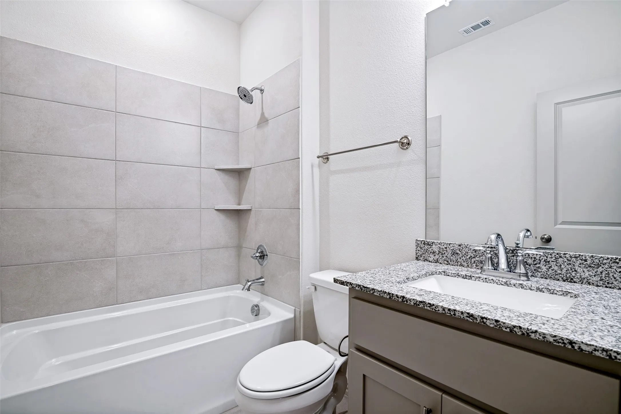 Bathroom featuring a bathtub with tiled surround and integrated shelving, granite-finish countertop, under-mount sink, and chrome fixtures