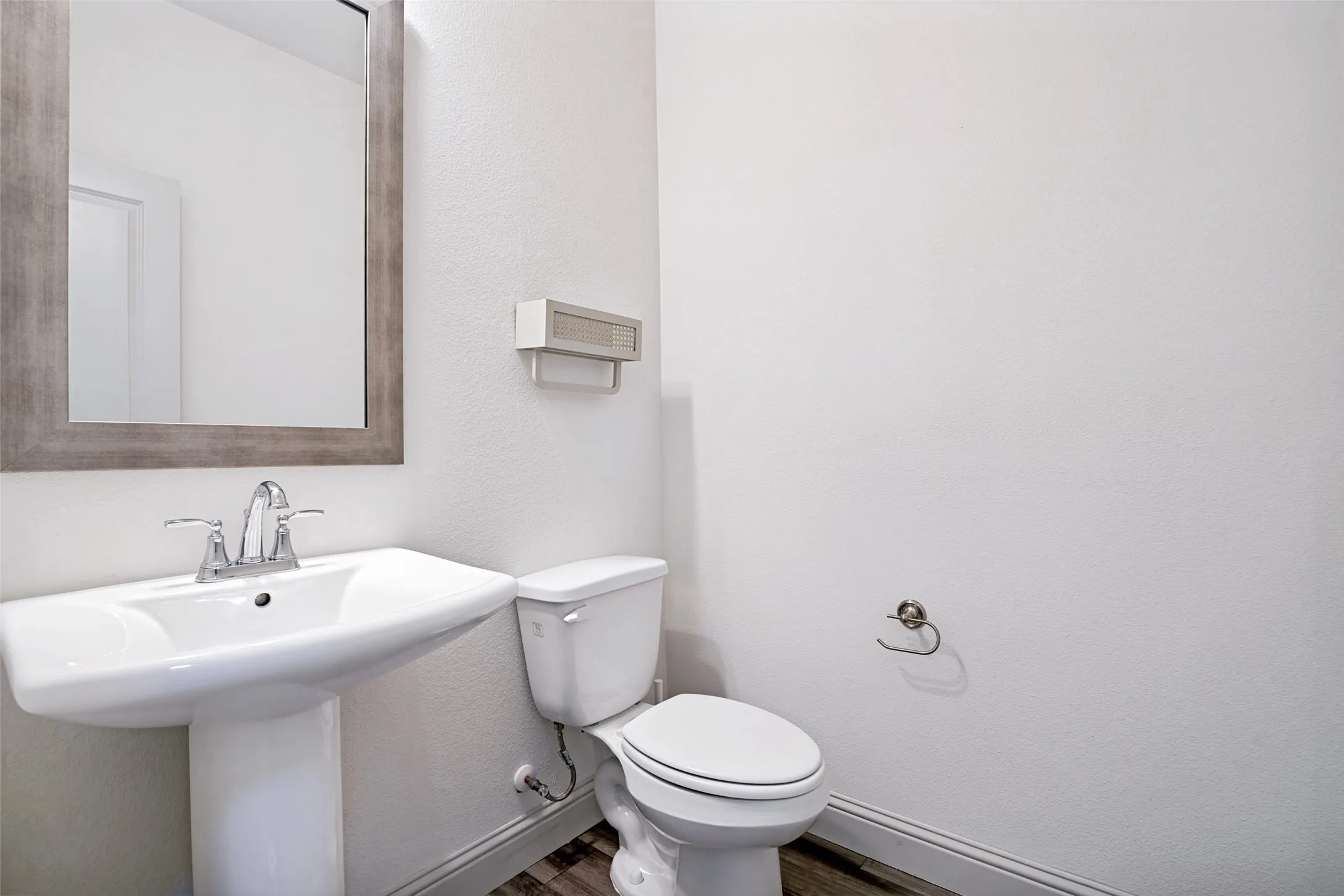 Pedestal sink with chrome faucet, framed mirror, and wood-finish flooring