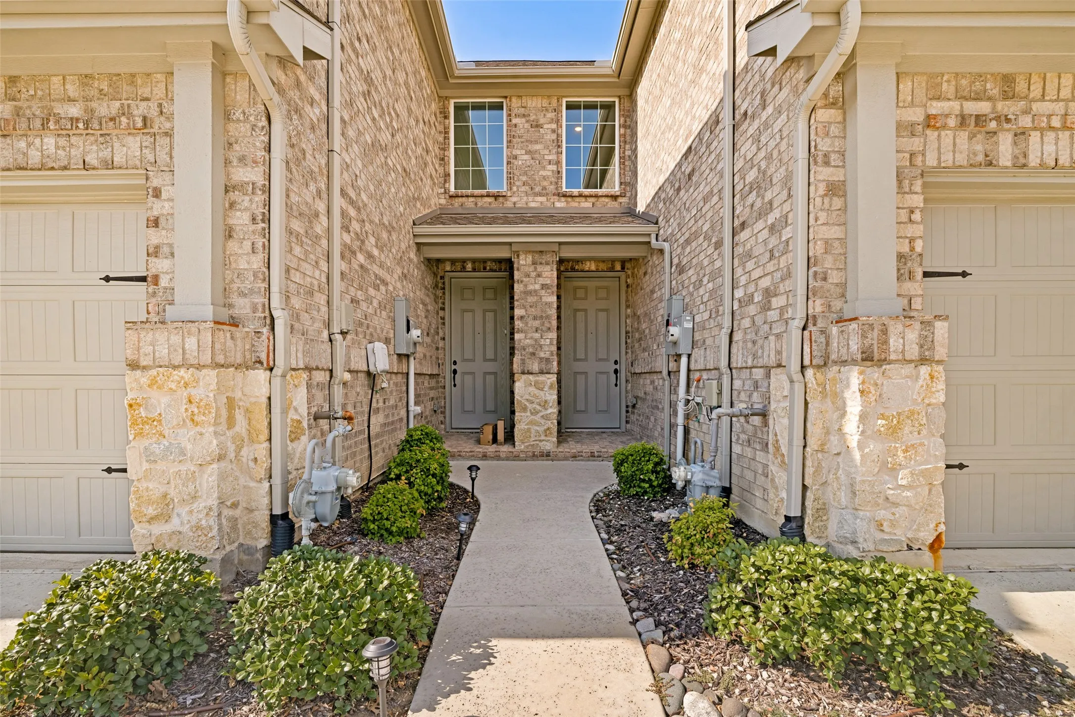 Brick exterior with stone accents, featuring two individual entry doors and two garage doors