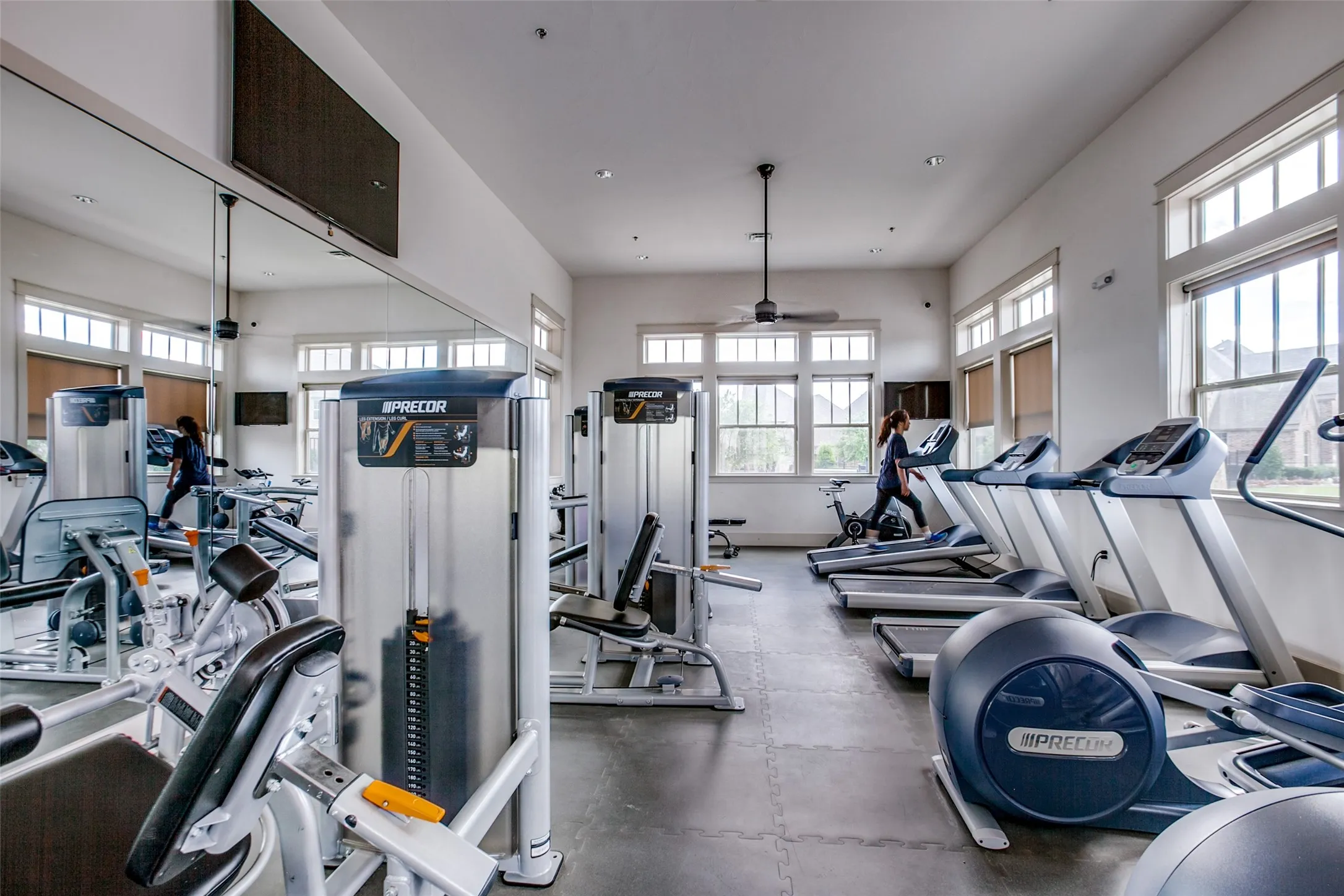 Fitness center featuring a mirrored wall, ample natural light from multiple windows, ceiling fan, and various exercise machines