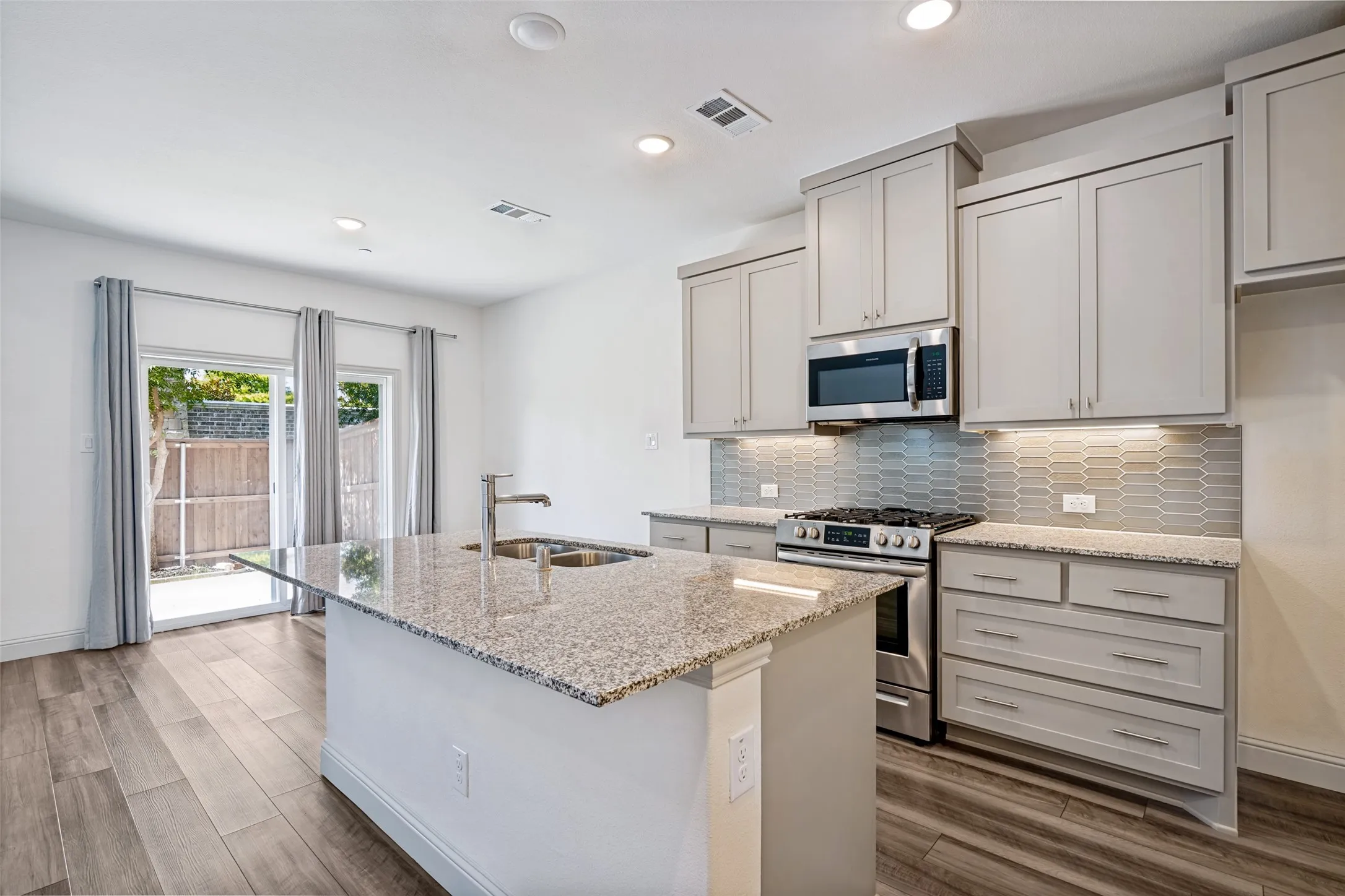 Modern kitchen featuring an island with a double basin sink, granite countertops, and stainless steel appliances