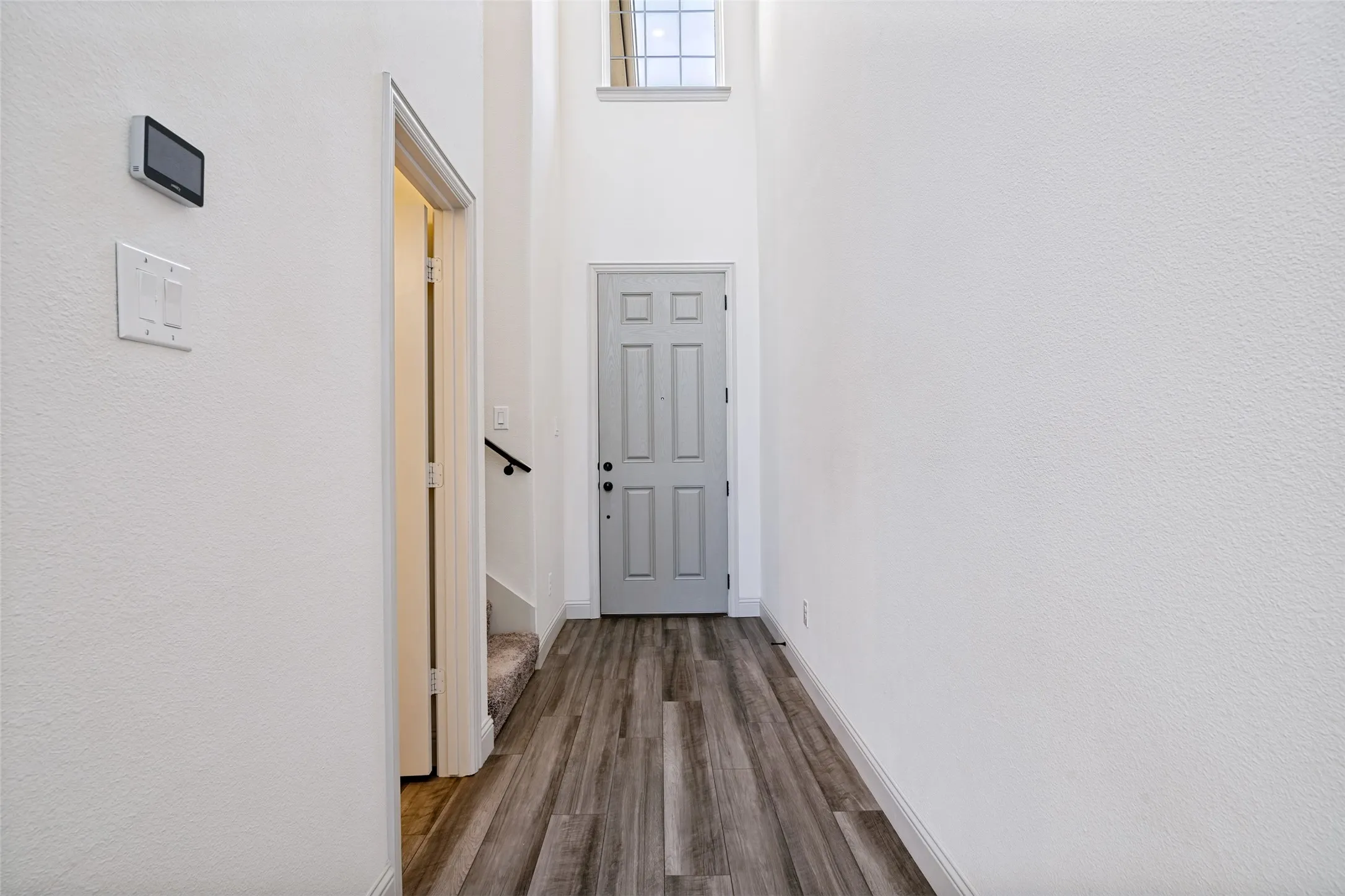 Foyer featuring high ceilings, wood-finish flooring, a light gray paneled door, and an upper window providing natural illumination