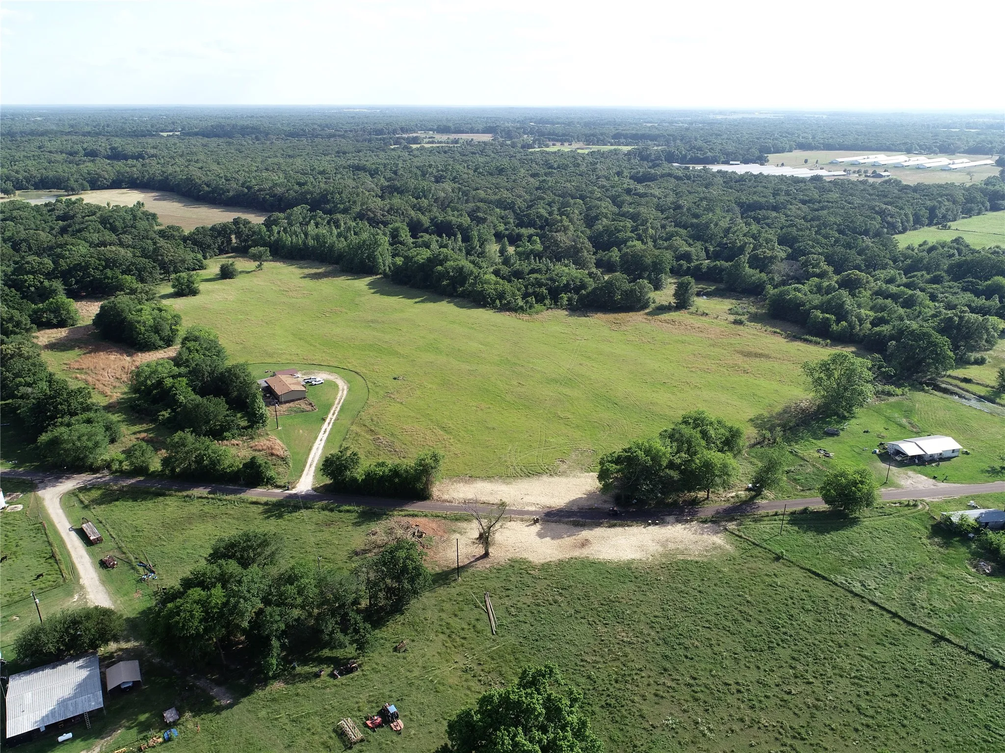 Expansive rural property featuring a main residence, additional structures, a winding driveway, and diverse terrain with open fields and wooded areas