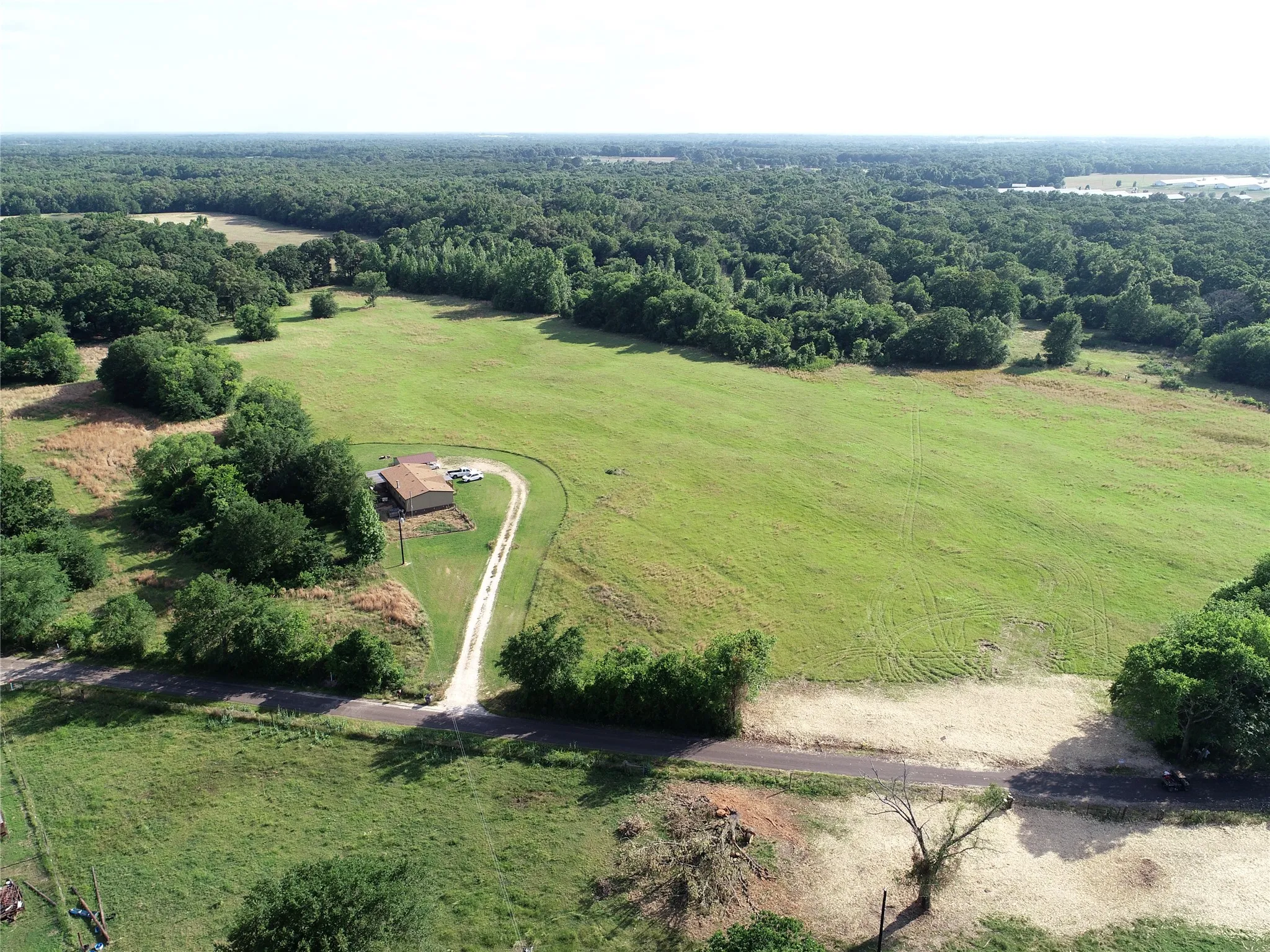 Expansive green acreage with a single-story structure featuring a brown roof