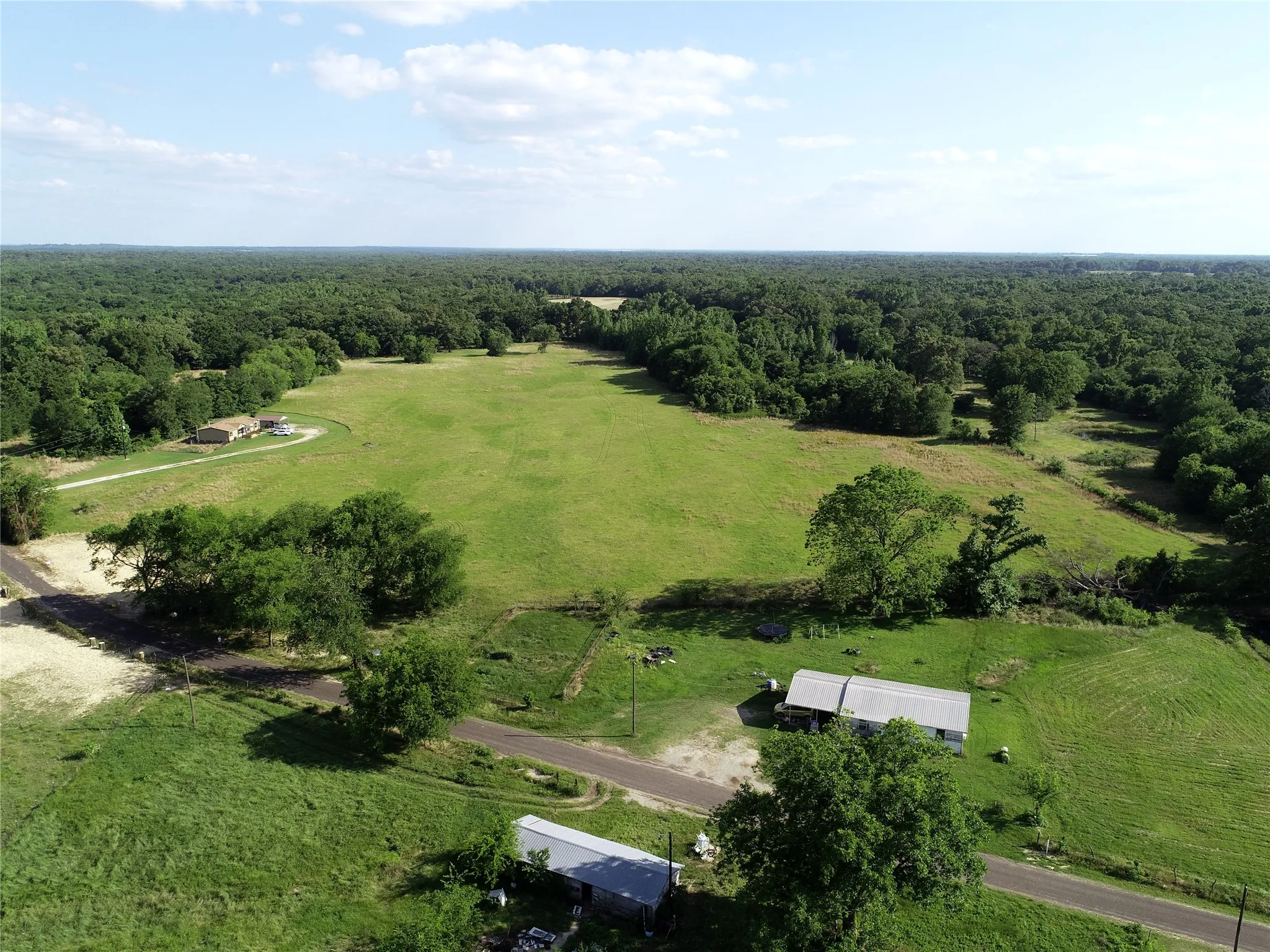 Expansive green acreage featuring a large open field, mature trees, and a distant single-story dwelling