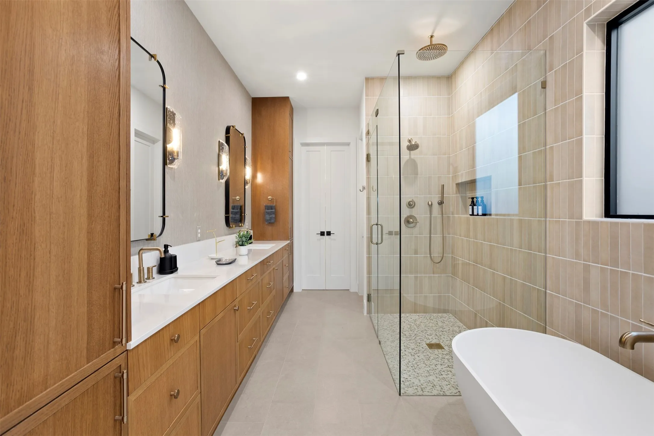 Spacious bathroom featuring a dual vanity with wood-finish cabinetry, quartz countertops, and modern brass fixtures