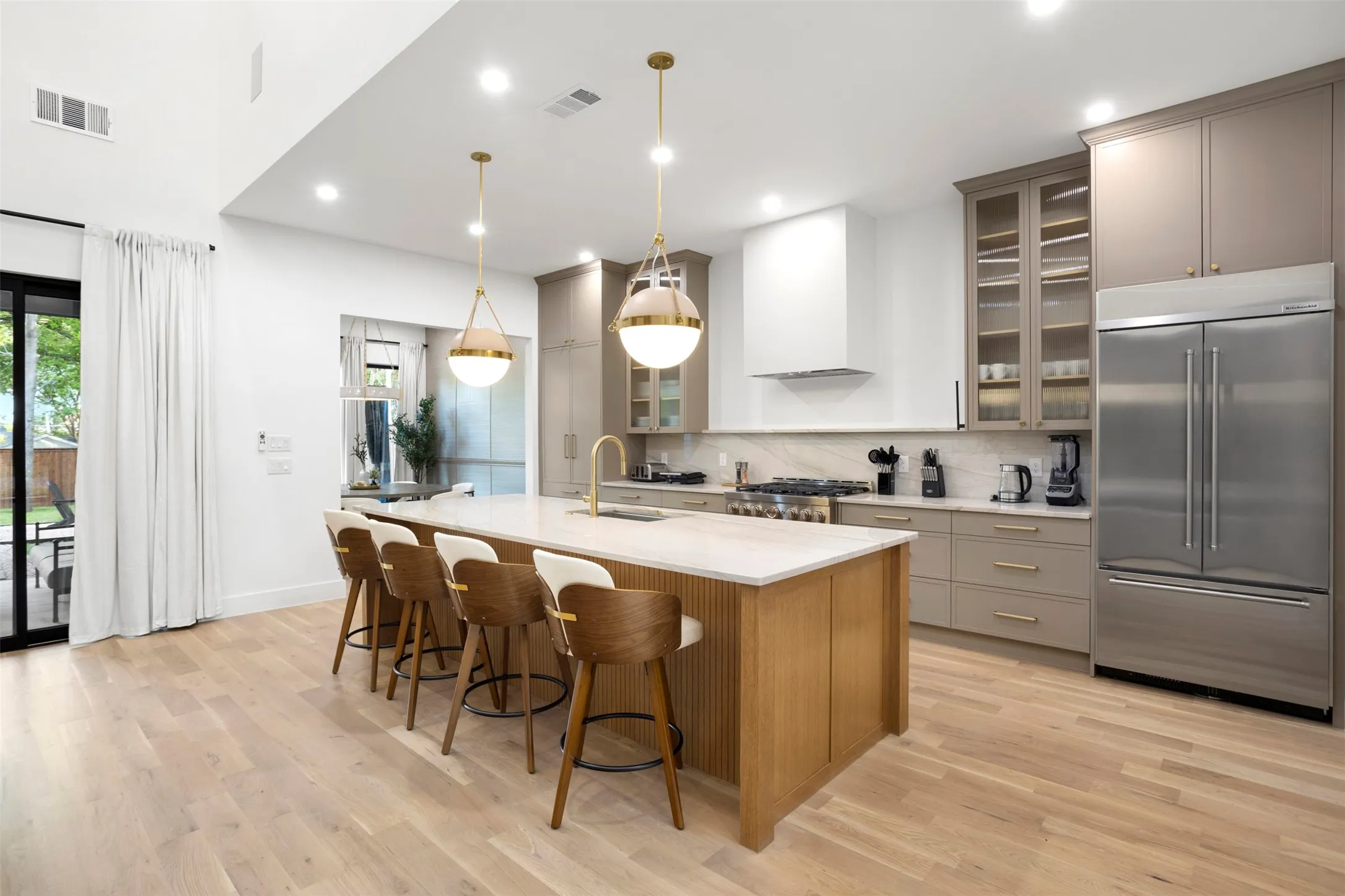 Spacious kitchen featuring a large central island with seating, integrated stainless steel appliances, light wood-finish flooring, and a vaulted ceiling