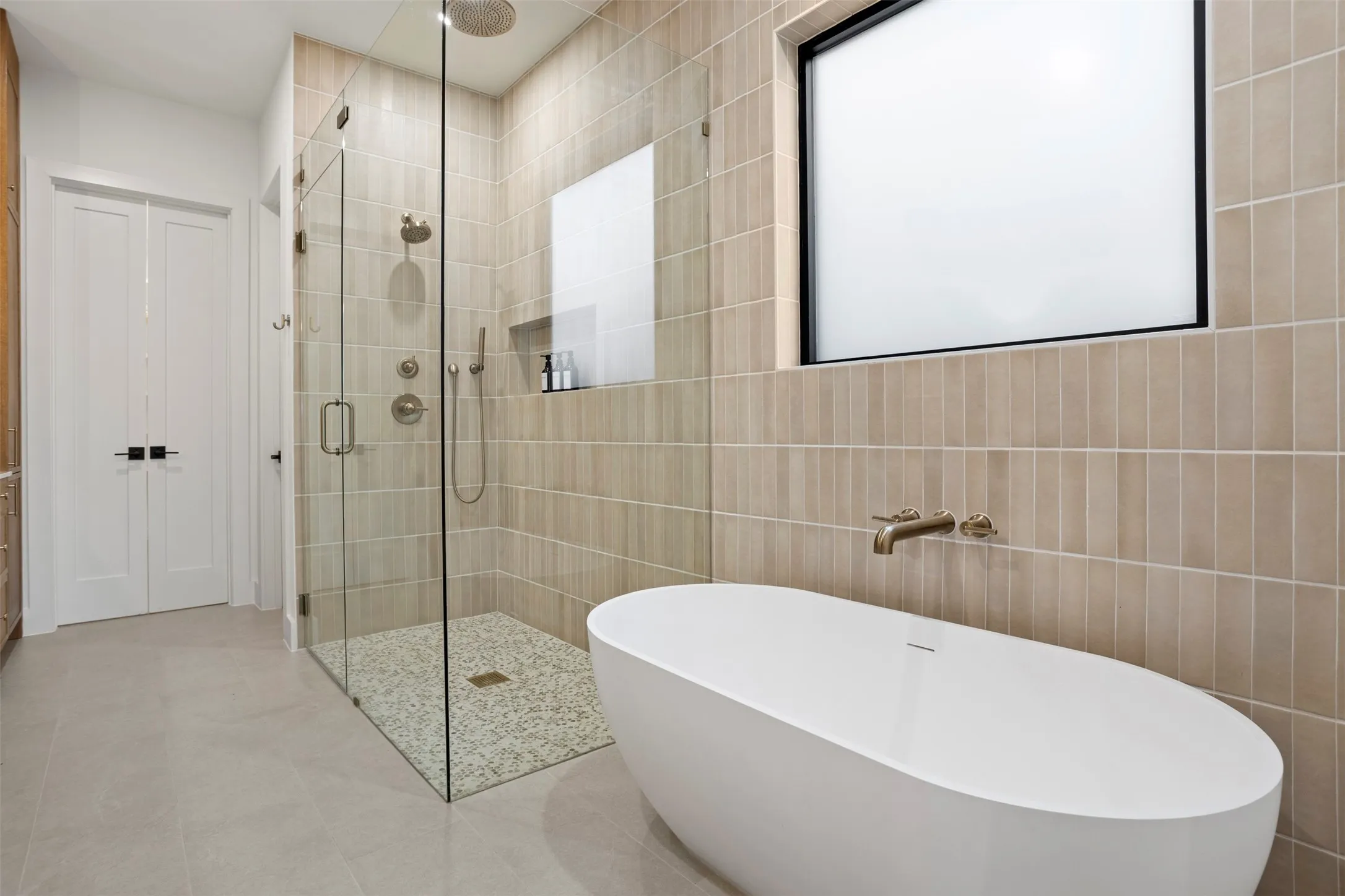 Modern bathroom featuring a freestanding soaking tub, a frameless glass shower enclosure with pebble flooring, and vertical tile accents