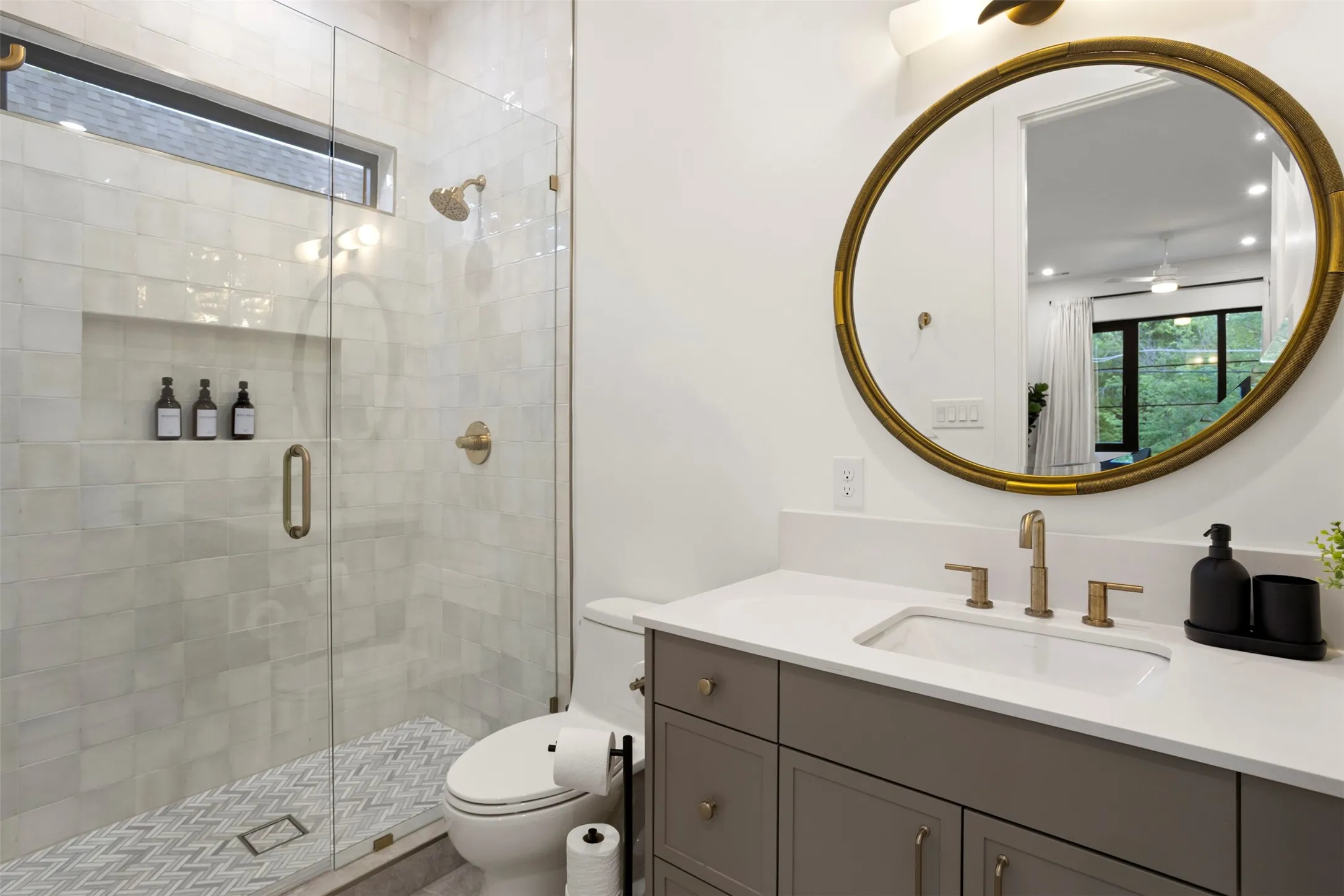 Well-appointed bathroom featuring a glass-enclosed shower with chevron-patterned floor tile, a single vanity with a white countertop, and a circular mirror with an ornate frame