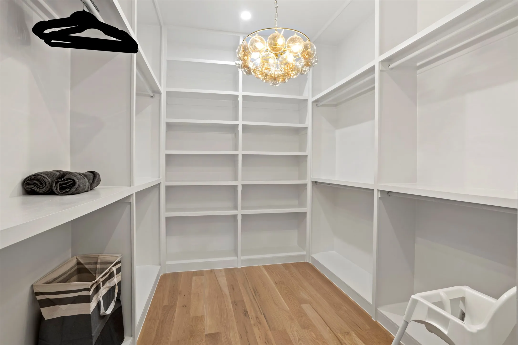 Walk-in closet featuring extensive built-in shelving, multiple hanging rods, warm wood-finish flooring, and an ornate ceiling light fixture