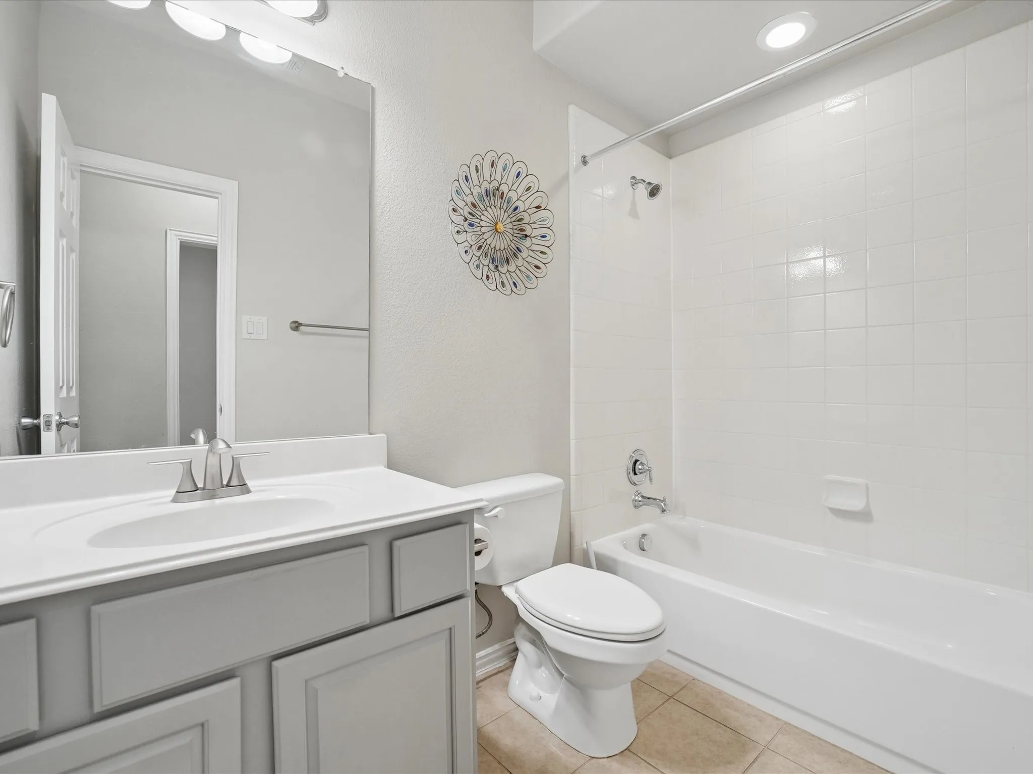 Bathroom featuring a light gray vanity with an integrated sink, a large wall-mounted mirror, white subway tile shower surround, and a built-in tub