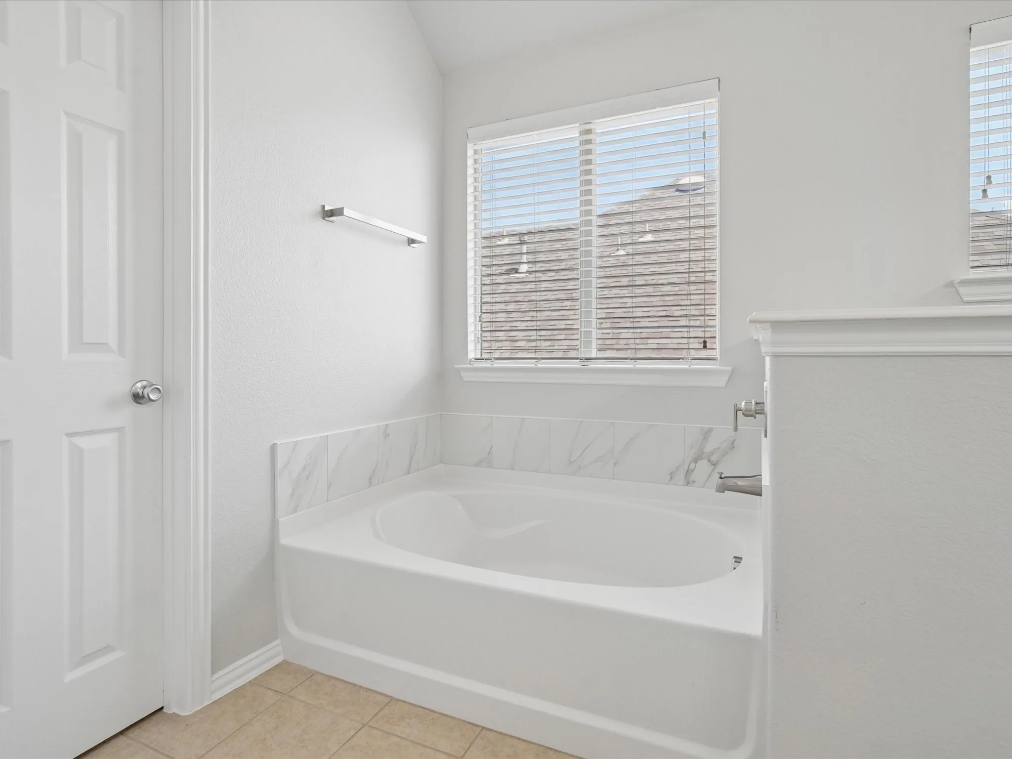 Deep-set tub with marble-look surround, chrome fixtures, and a window with blinds