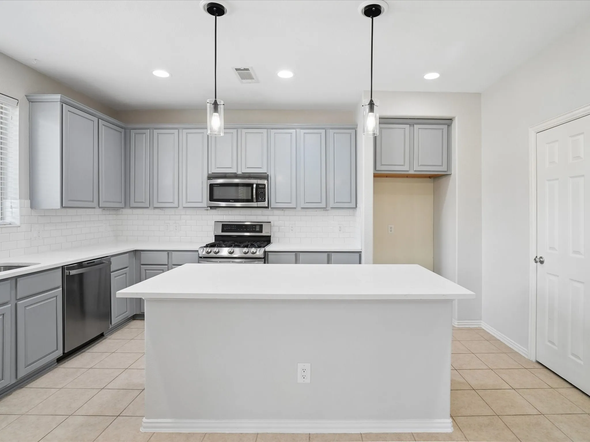 Kitchen featuring a central island with a solid surface countertop, gray cabinetry, stainless steel appliances, a subway tile backsplash, and recessed lighting