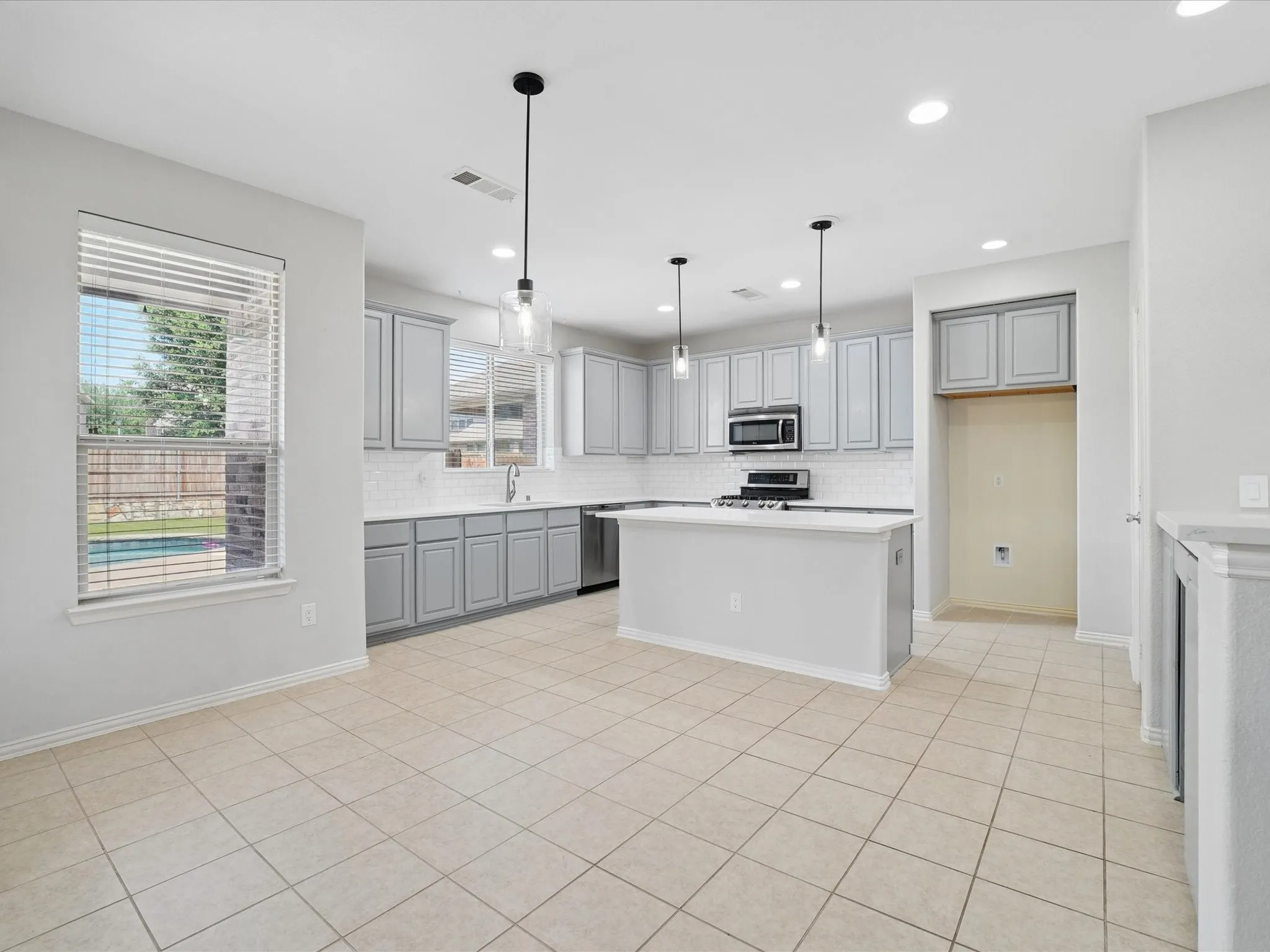 Open-concept kitchen featuring an island with counter seating, light gray cabinetry, stainless steel appliances, a white subway tile backsplash, and light-toned tile flooring