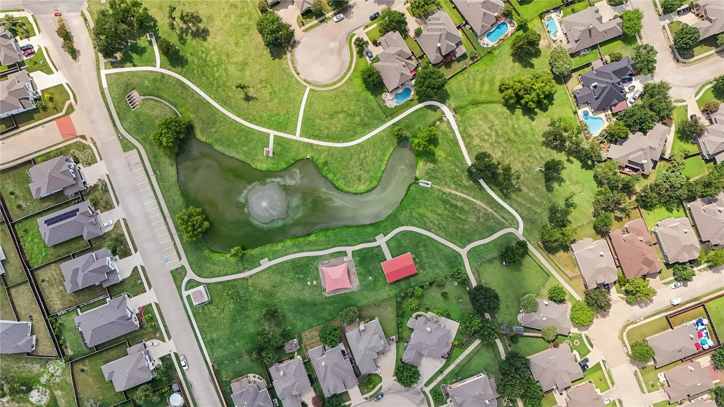 Expansive green space featuring a pond with a fountain, paved walking paths, multiple picnic structures, and surrounding residential properties
