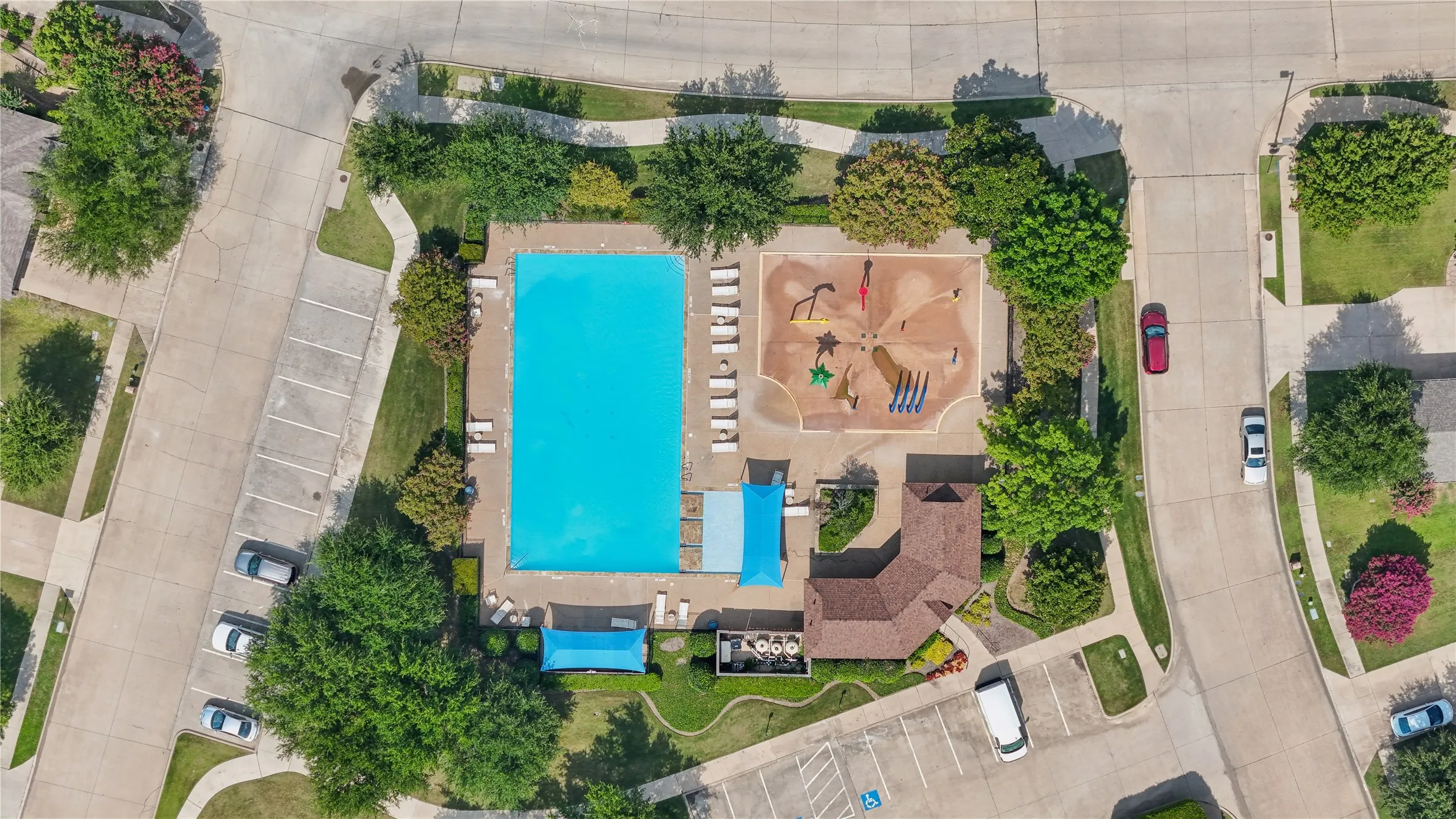 Community swimming pool with surrounding paved deck, water play area, and adjacent clubhouse
