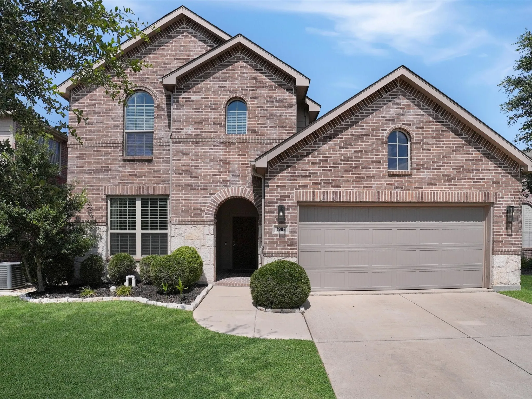 Brick and stone façade featuring an arched entryway, gabled rooflines, and arched windows