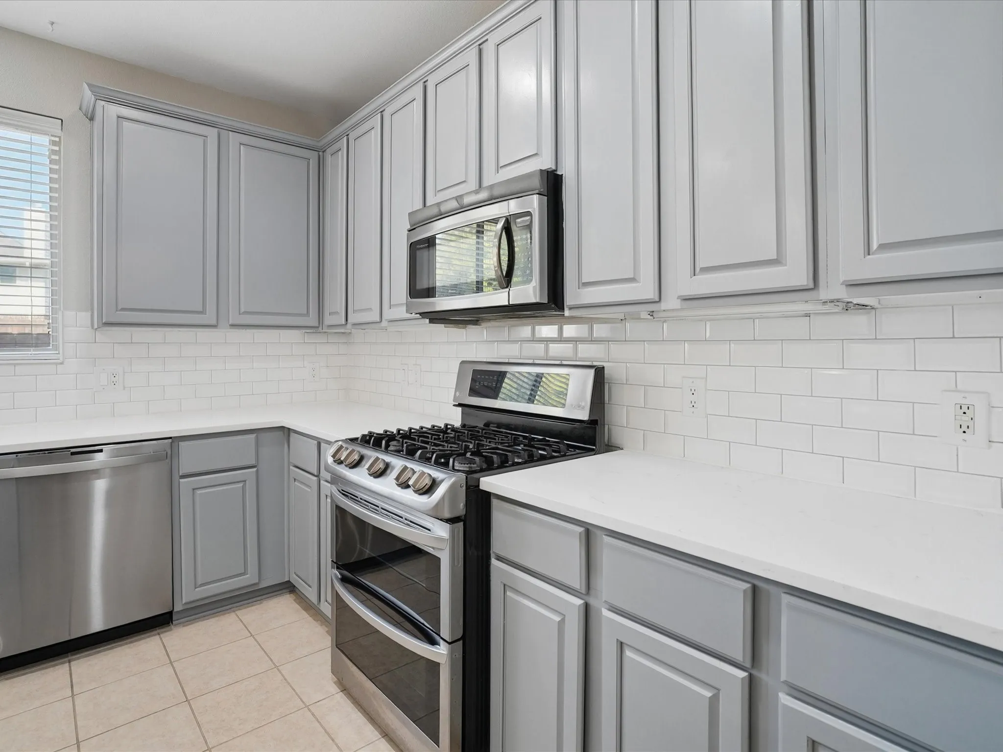 Kitchen featuring grey shaker-style cabinetry, white subway tile backsplash, stainless steel appliances, and light-toned countertops