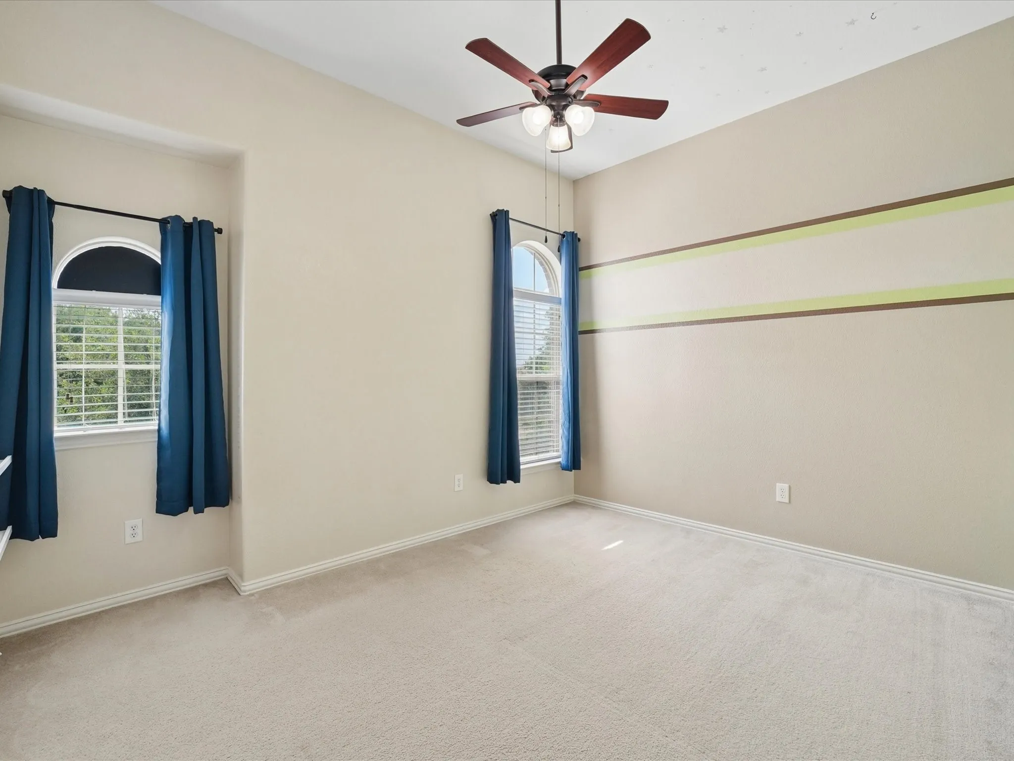 Carpeted room featuring dual arched windows, a multi-blade ceiling fan with integrated lighting, and neutral wall tones with decorative banding