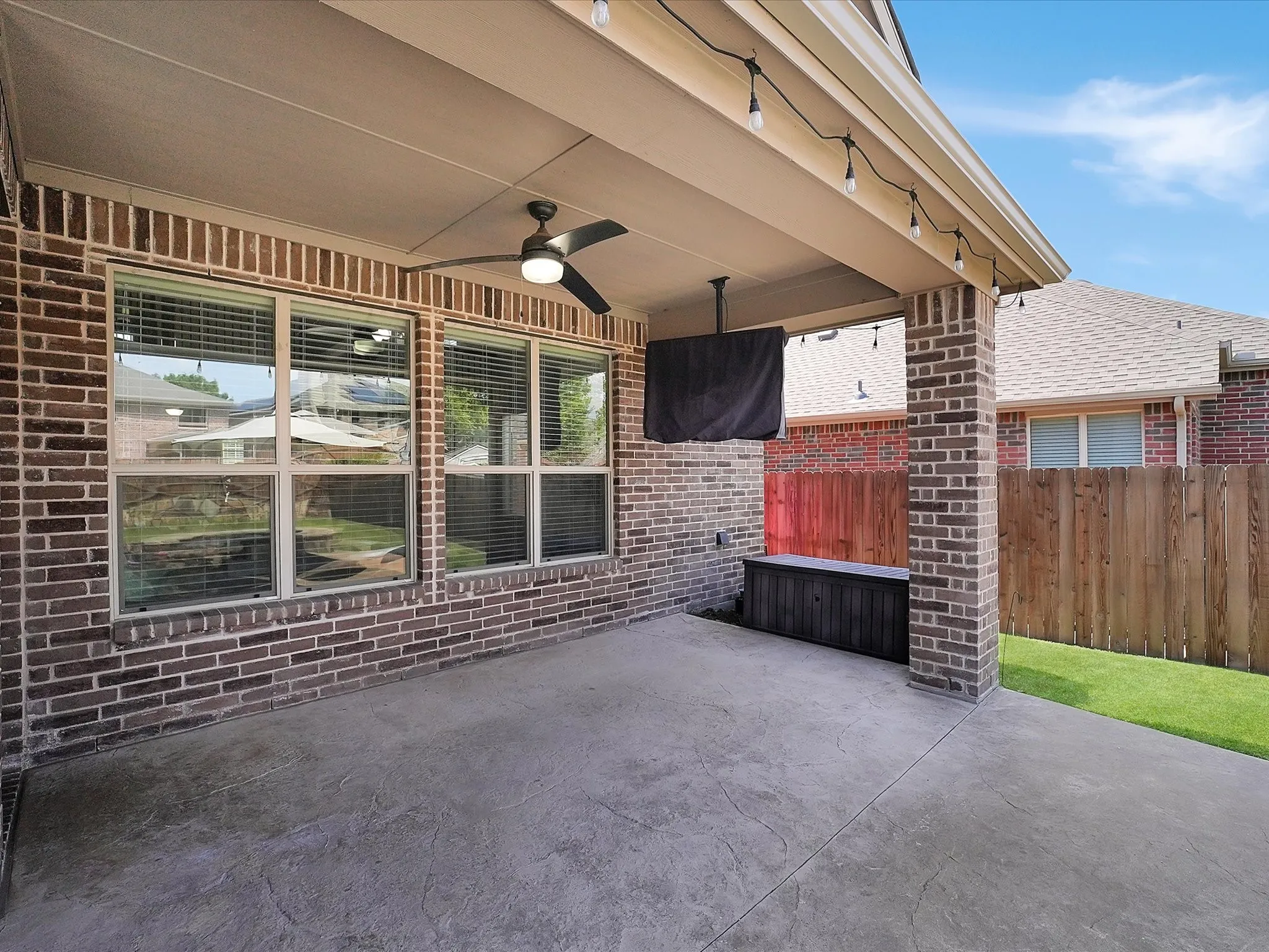Covered patio featuring an embossed concrete floor, brick columns, string lighting, and a ceiling fan