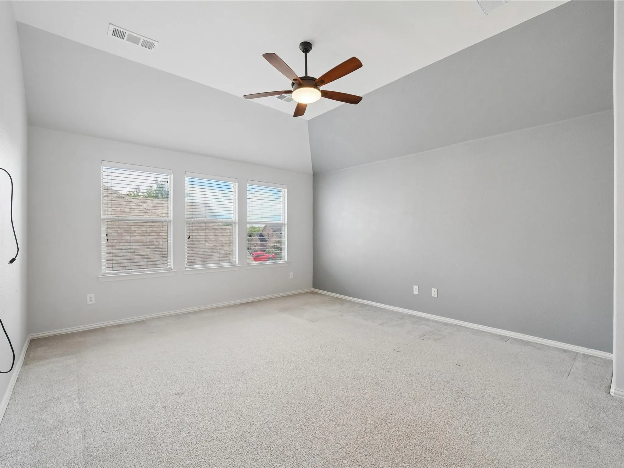 Spacious room featuring vaulted ceilings, a ceiling fan with light fixture, light gray walls, and plush carpeting