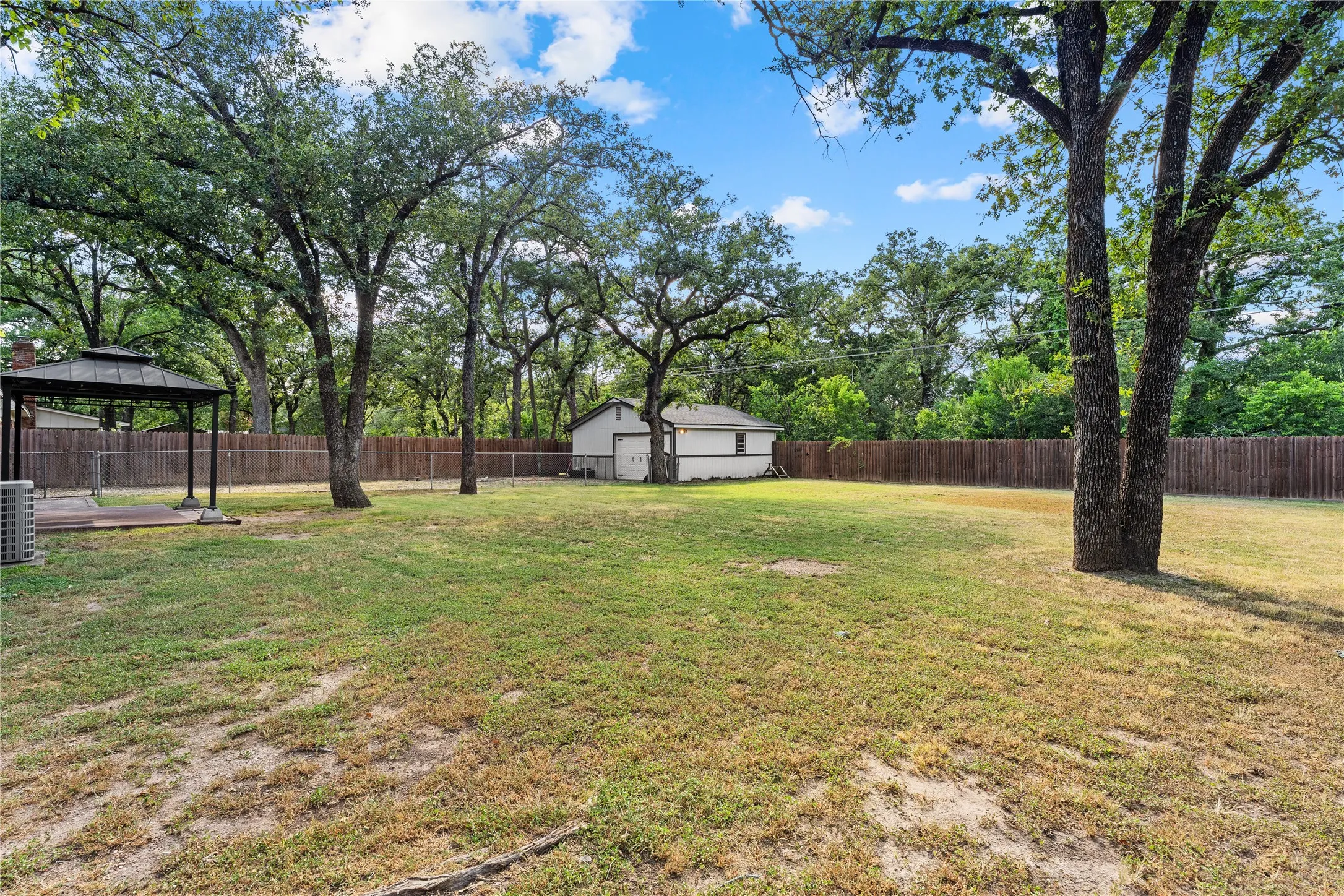 Spacious backyard featuring mature trees, a wooden privacy fence, and a gazebo with a built-in deck
