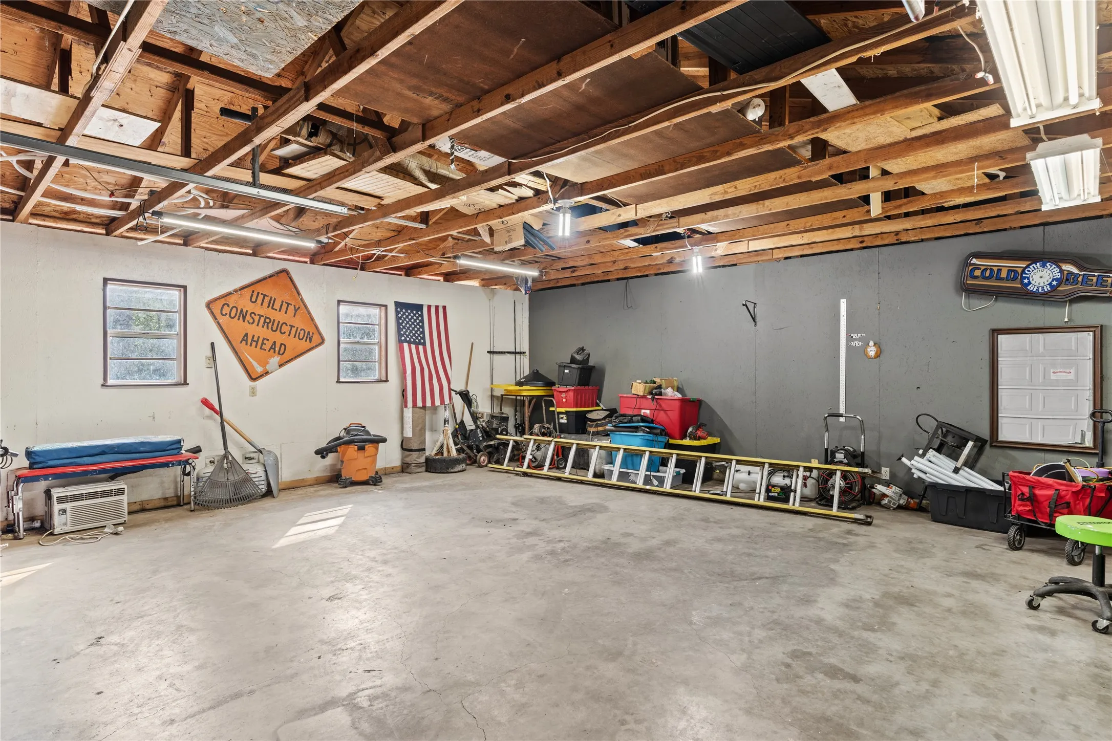 Spacious concrete-floored interior featuring exposed wood beam ceiling, multiple windows, and extensive overhead lighting