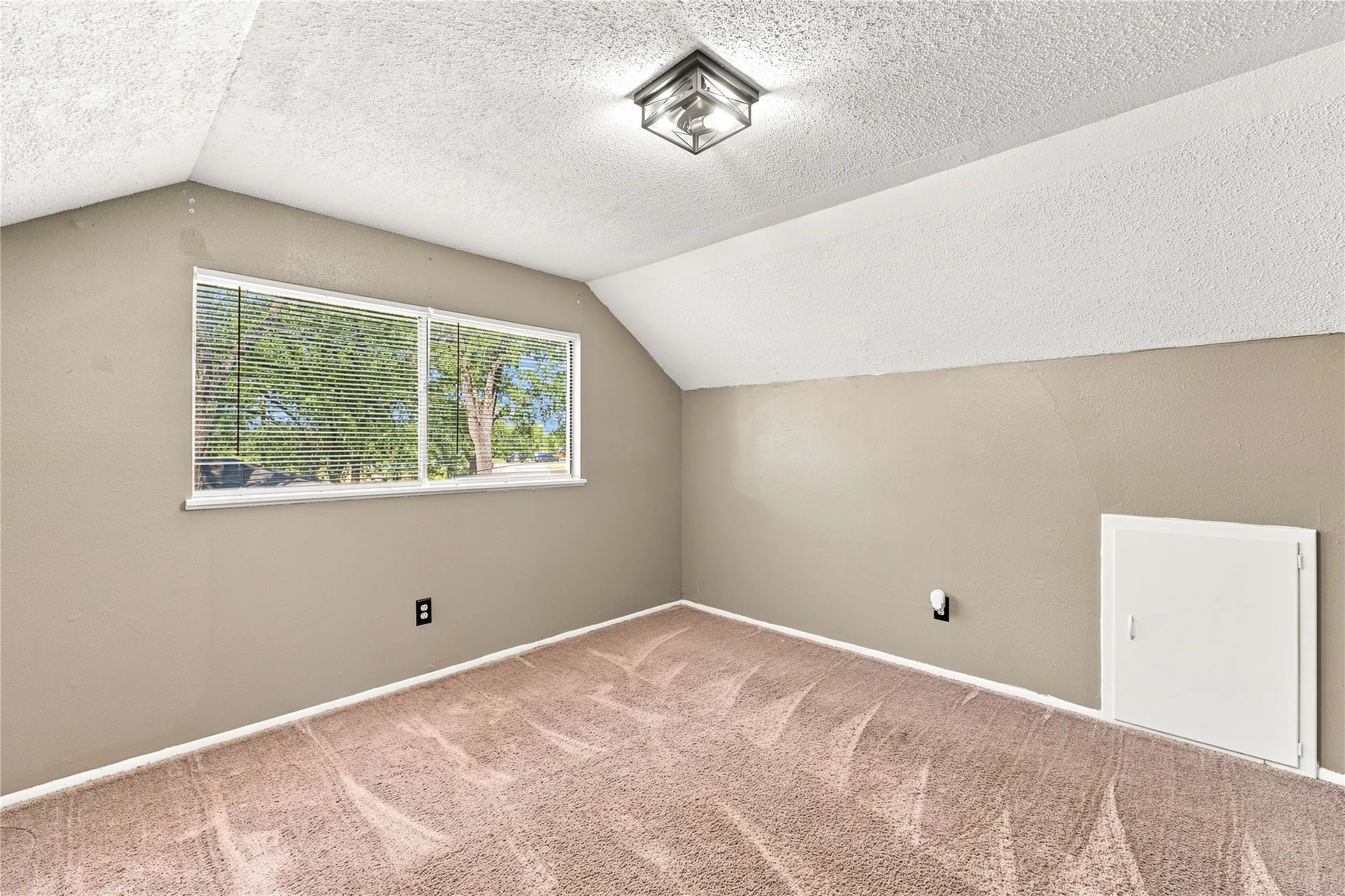Sloped ceiling room featuring a flush-mount ceiling light fixture, twin window with blinds, and carpet flooring