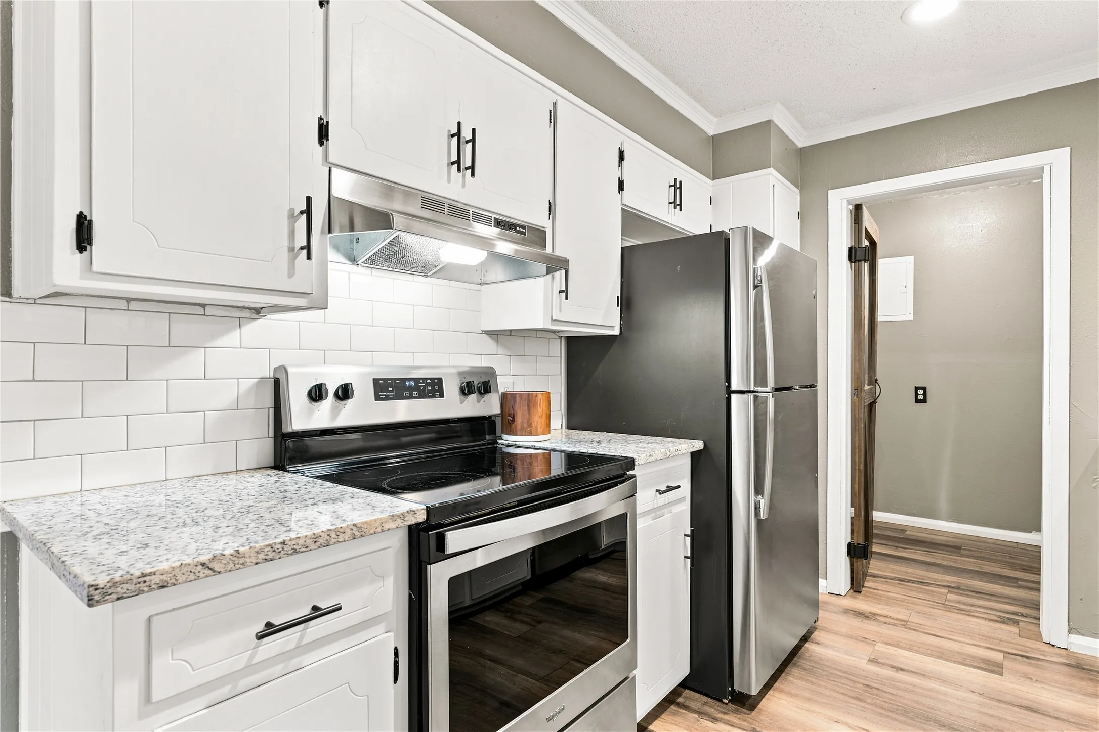 Kitchen featuring stainless steel appliances, granite-style countertops, white subway tile backsplash, white cabinetry with black hardware, and wood-finish flooring