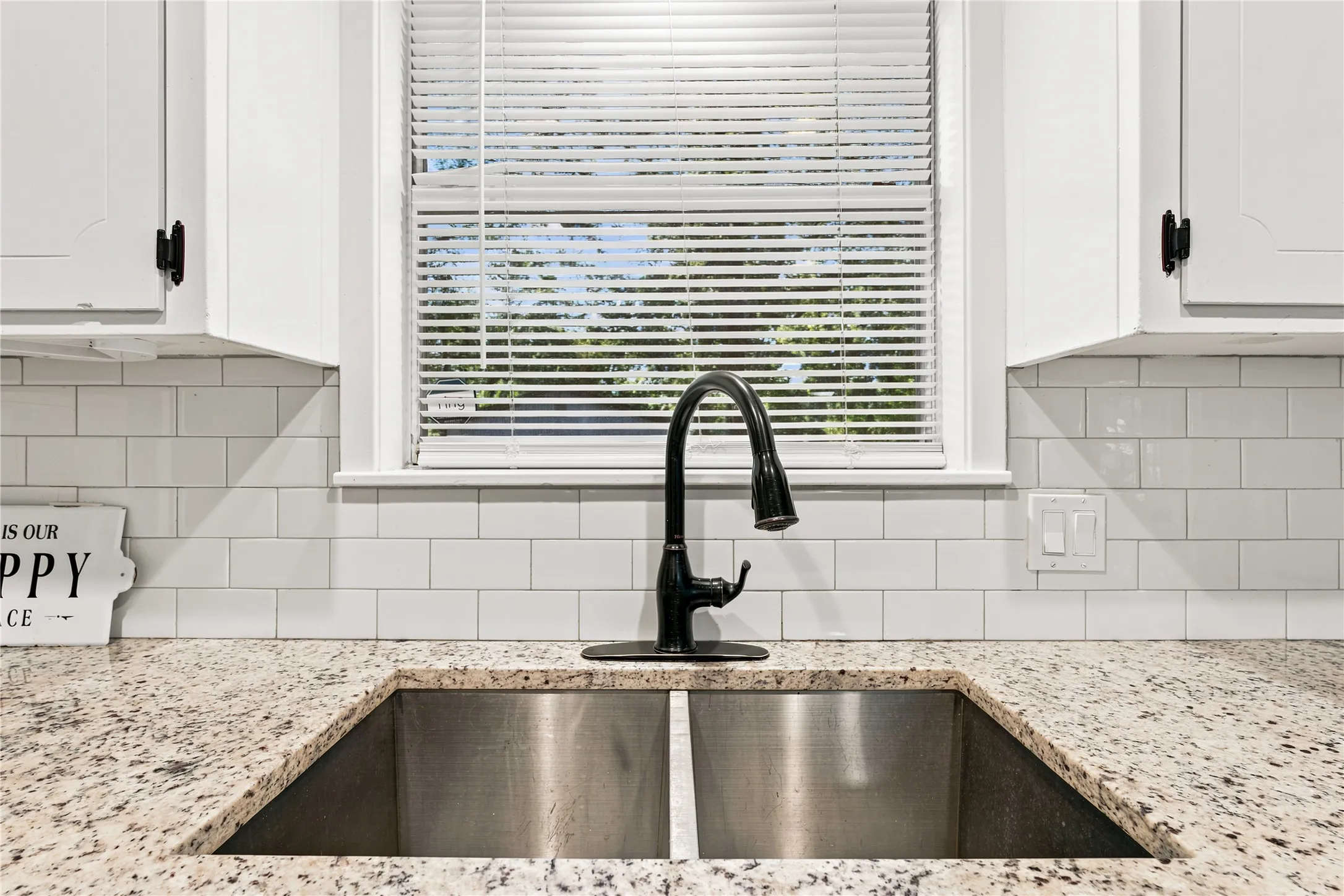 Kitchen workstation featuring a dual-basin stainless steel sink, speckled countertop, and subway tile backsplash
