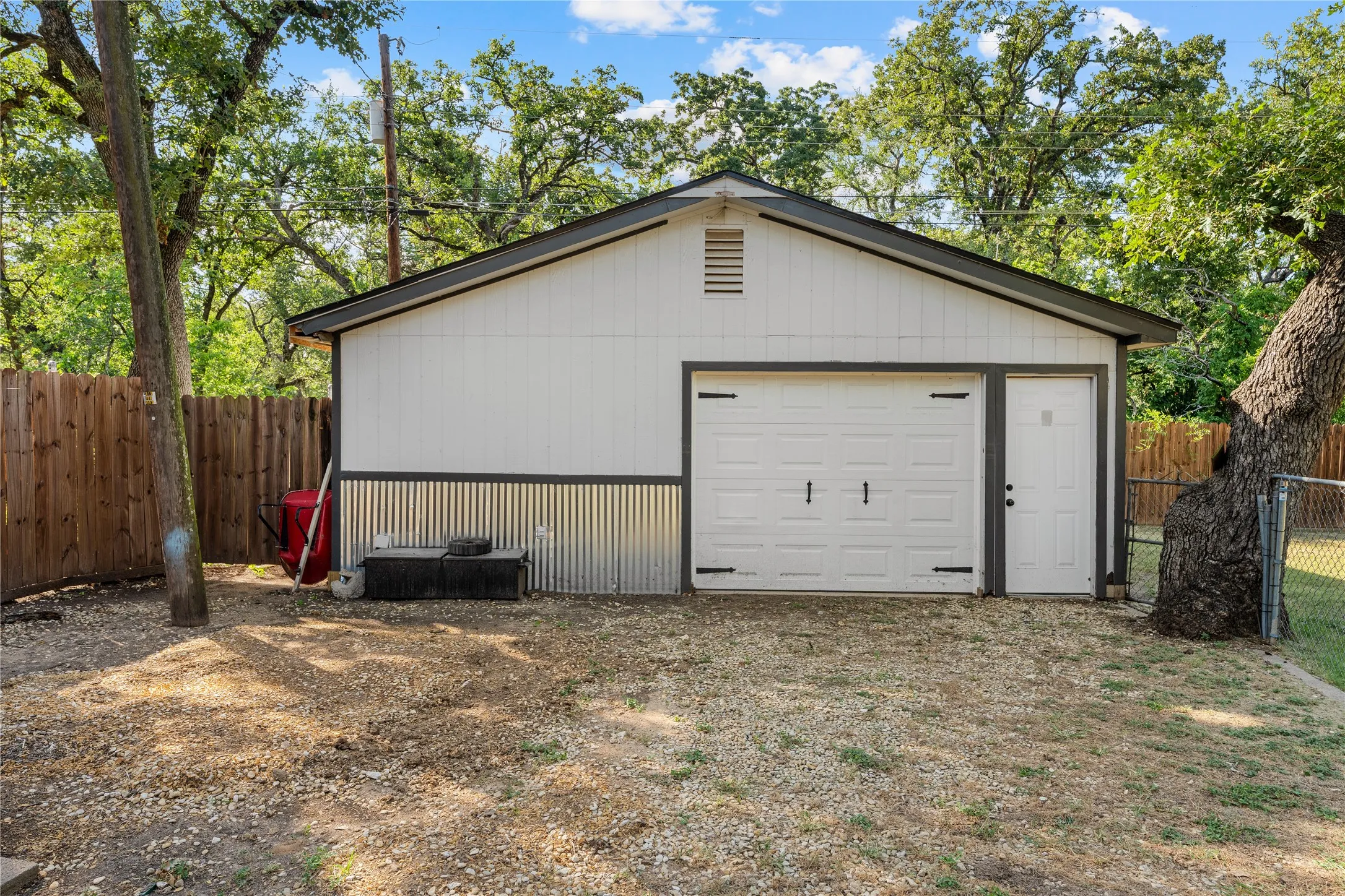 Detached accessory building featuring white vertical siding and corrugated metal paneling
