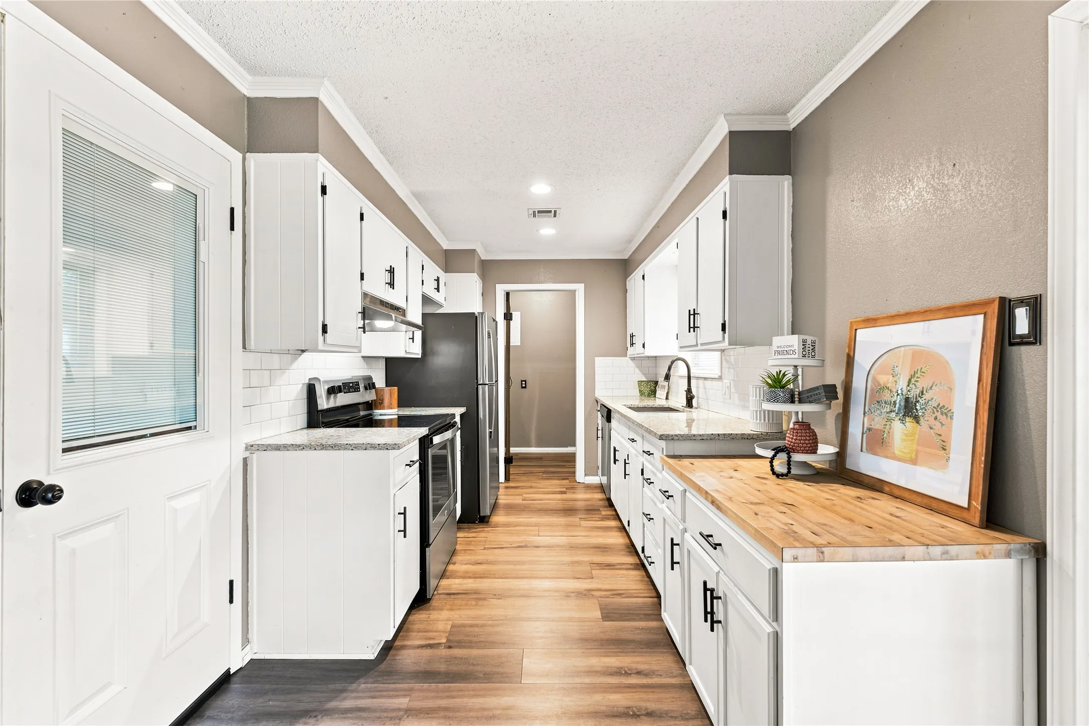 Galley kitchen featuring white cabinetry, granite countertops, wood-finish flooring, a subway tile backsplash, and stainless steel appliances
