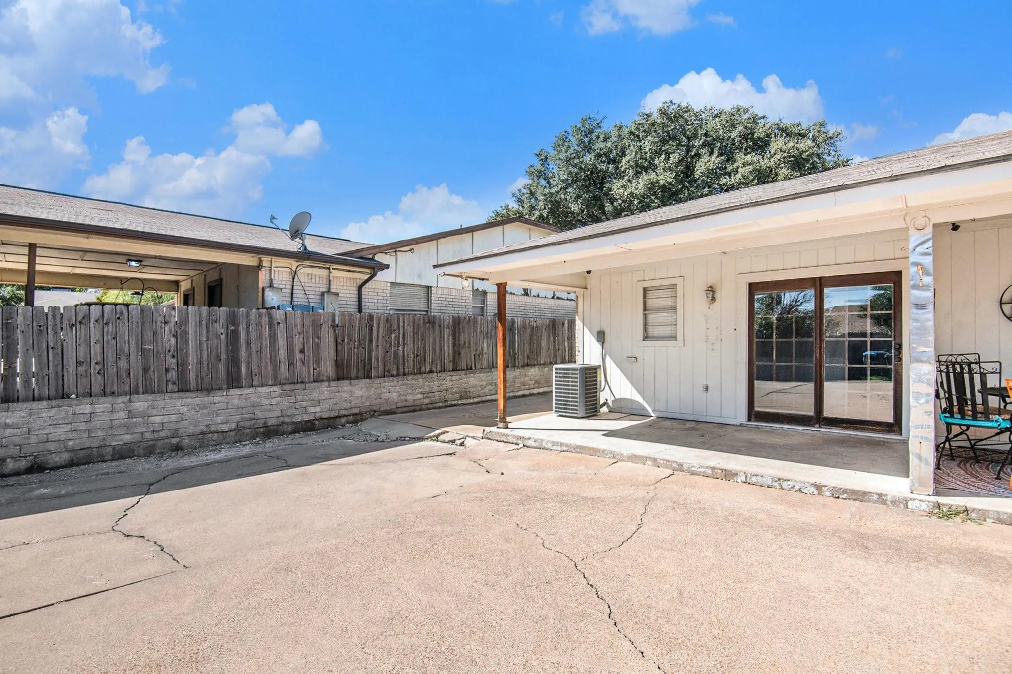 Rear property exterior featuring a concrete patio, sliding glass doors, and a partial wood fence over a stone-finish retaining wall